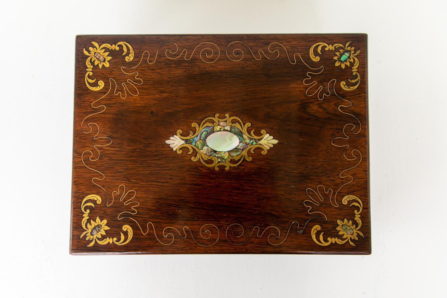 Rosewood inlaid jewelry box, inlaid with engraved brass panels and abalone shells and is framed with brass wire arabesques. The interior has a removable tray with multiple compartments, and is covered with cobalt blue fabric lined with silver foil.