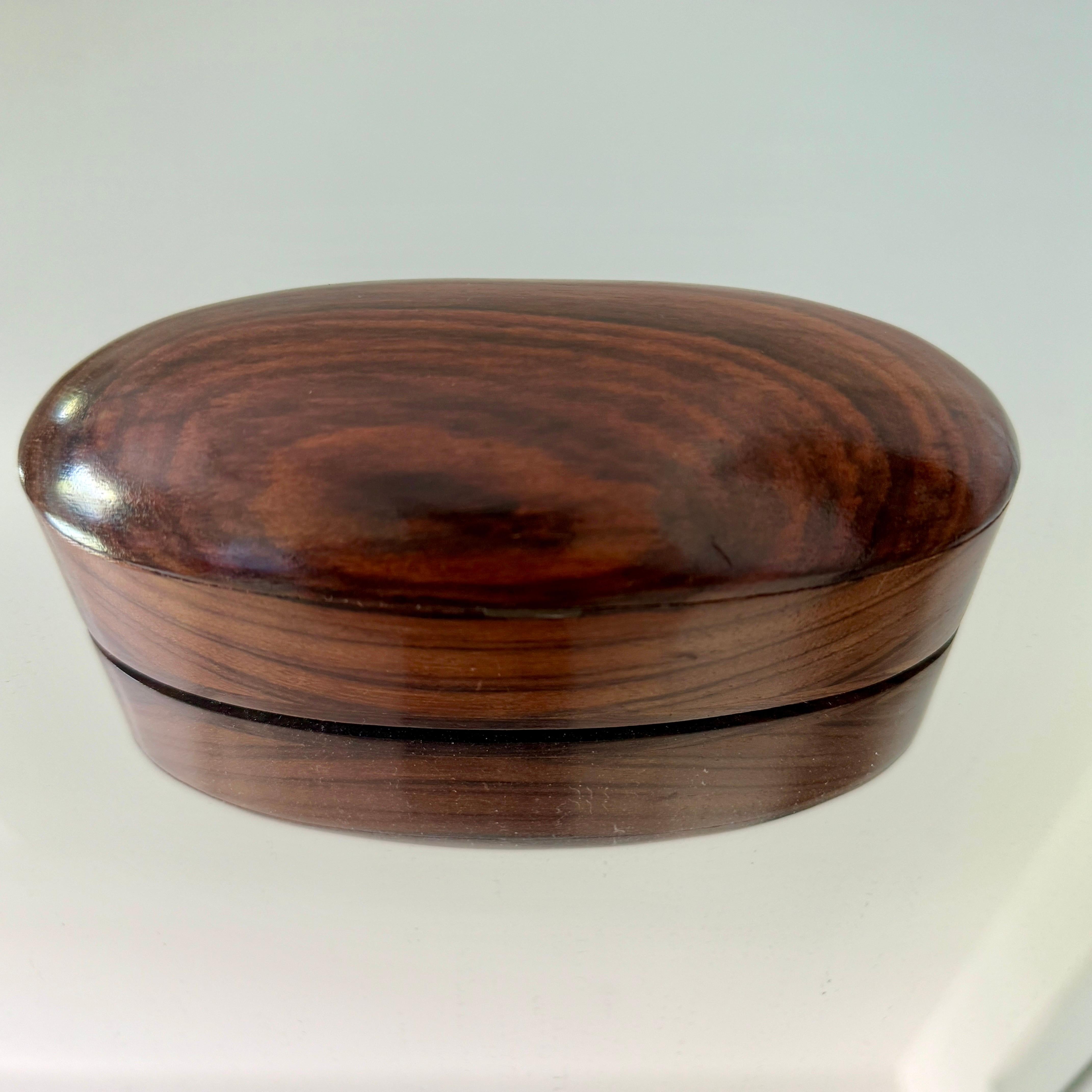 Rosewood box with streamlined minimalist design.  Handcrafted with an oval shape and a turned wood lid.  Makes a handsome decorative object for a desk or coffee table. 