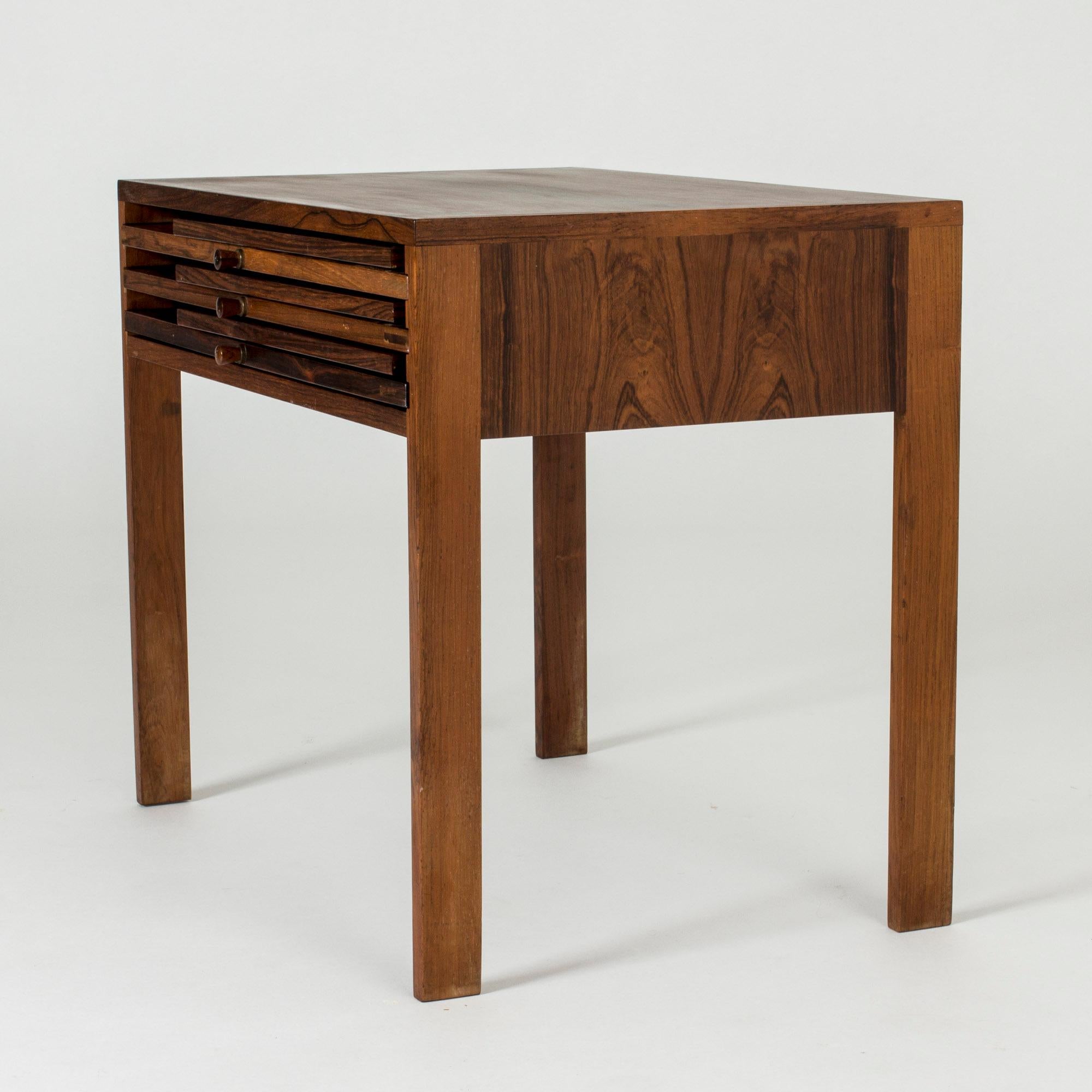 Rosewood nesting table in a clever and very elegant design by Illum Wikkelsø. Three small folding tables are stacked like cassettes inside the table and are pulled out with small knobs that also make a decorative detail. Very nice craftsmanship.