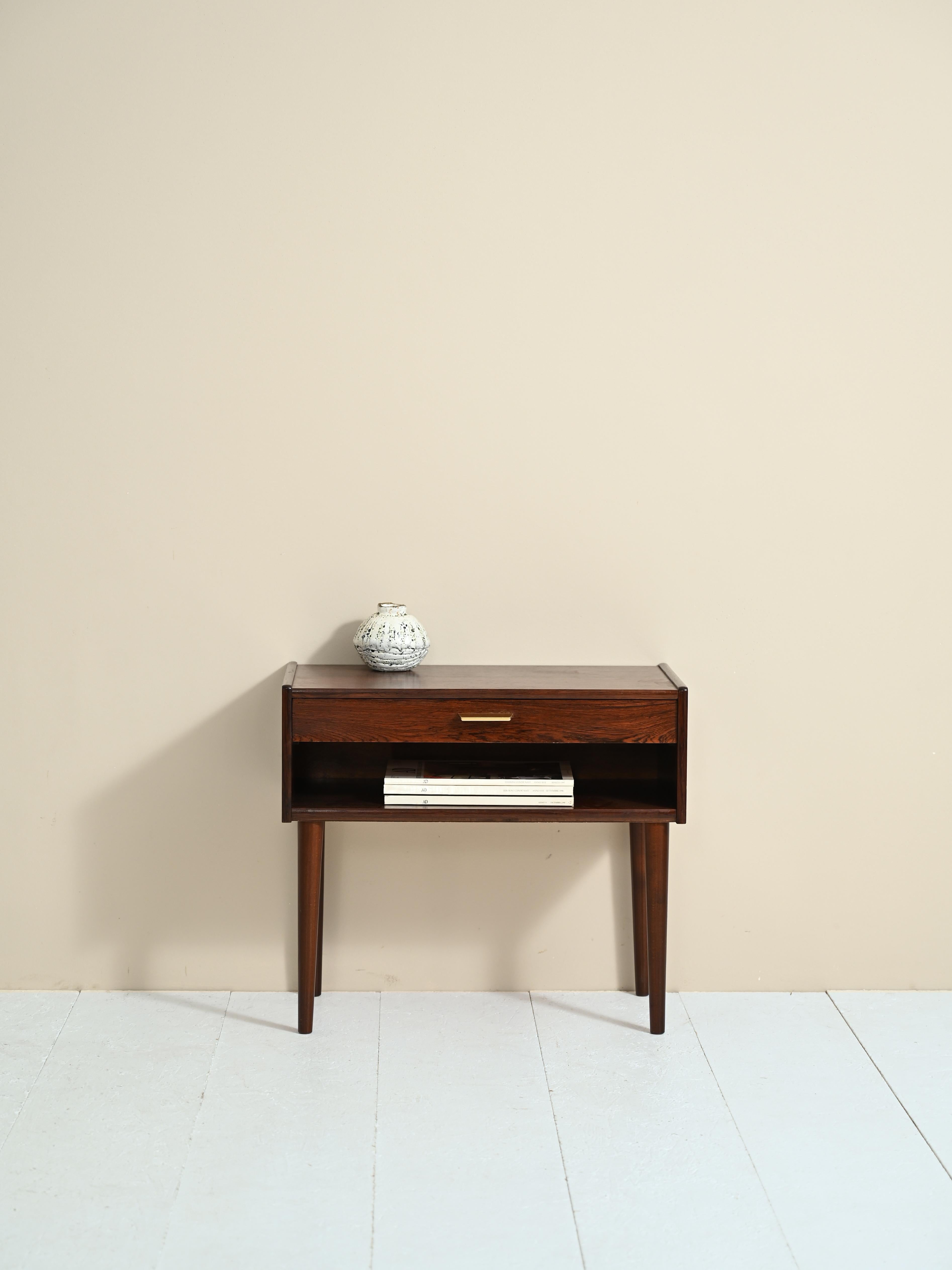 Scandinavian cabinet produced by Möblerfabrik in the 1960s.
There is a magazine rack top and a drawer with a gold metal handle. Tapered legs slender the frame. 
Deeply colored and markedly grained rosewood makes this bedside table a valuable and