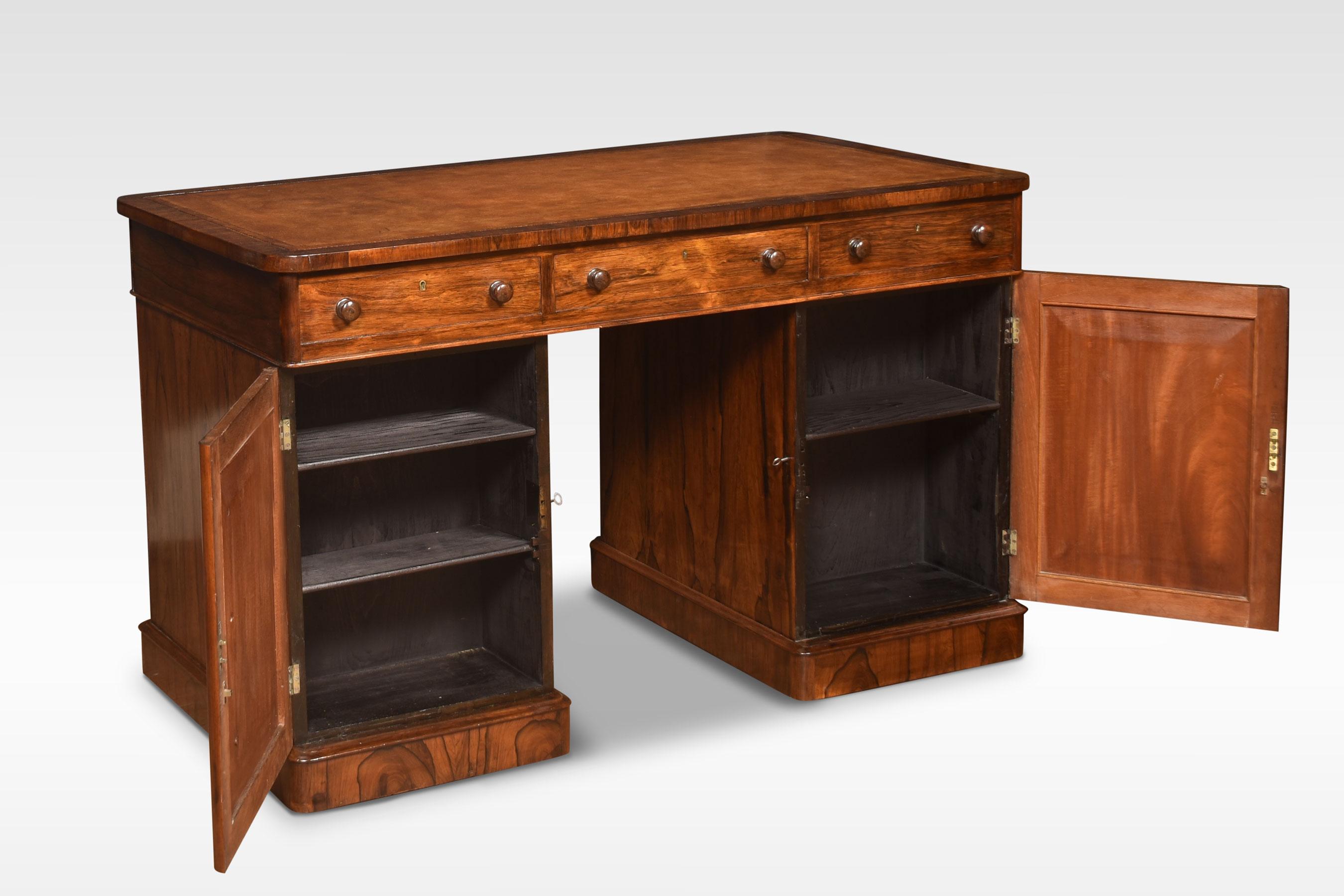 Twin pedestal desk, the moulded square edge top, inset with inset tooled hide, above one large and two short frieze drawers. the pedestals with an arrangement of graduated drawers, and the opposing side fitted with cupboards. All fitted with turned