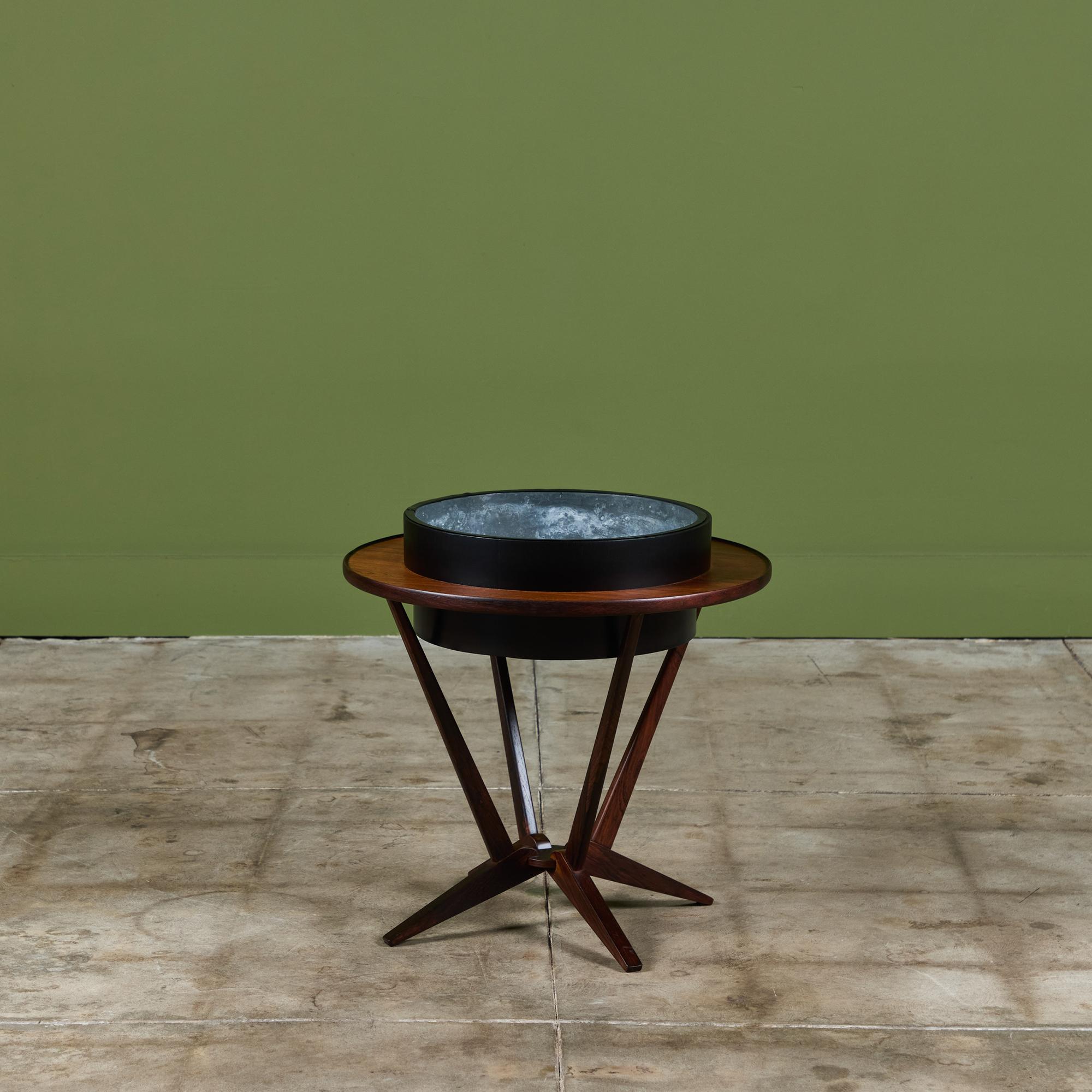 Jardinière ronde en bois de rose avec bol central émaillé noir pour la plante. Cette pièce a un bord plat en palissandre et quatre supports qui s'affinent vers le bas du support et s'évasent ensuite vers quatre pieds.

Avis de cites : En raison de