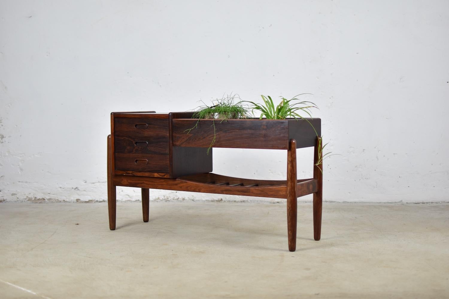 This entry chest was designed by Arne Wahl Iversen for Vamo Møbelfabrik, Denmark 1961. It features a chest of three drawers on the left and a low slated magazine shelf under the planter area, all in rosewood. Finished back, allowing it to be placed