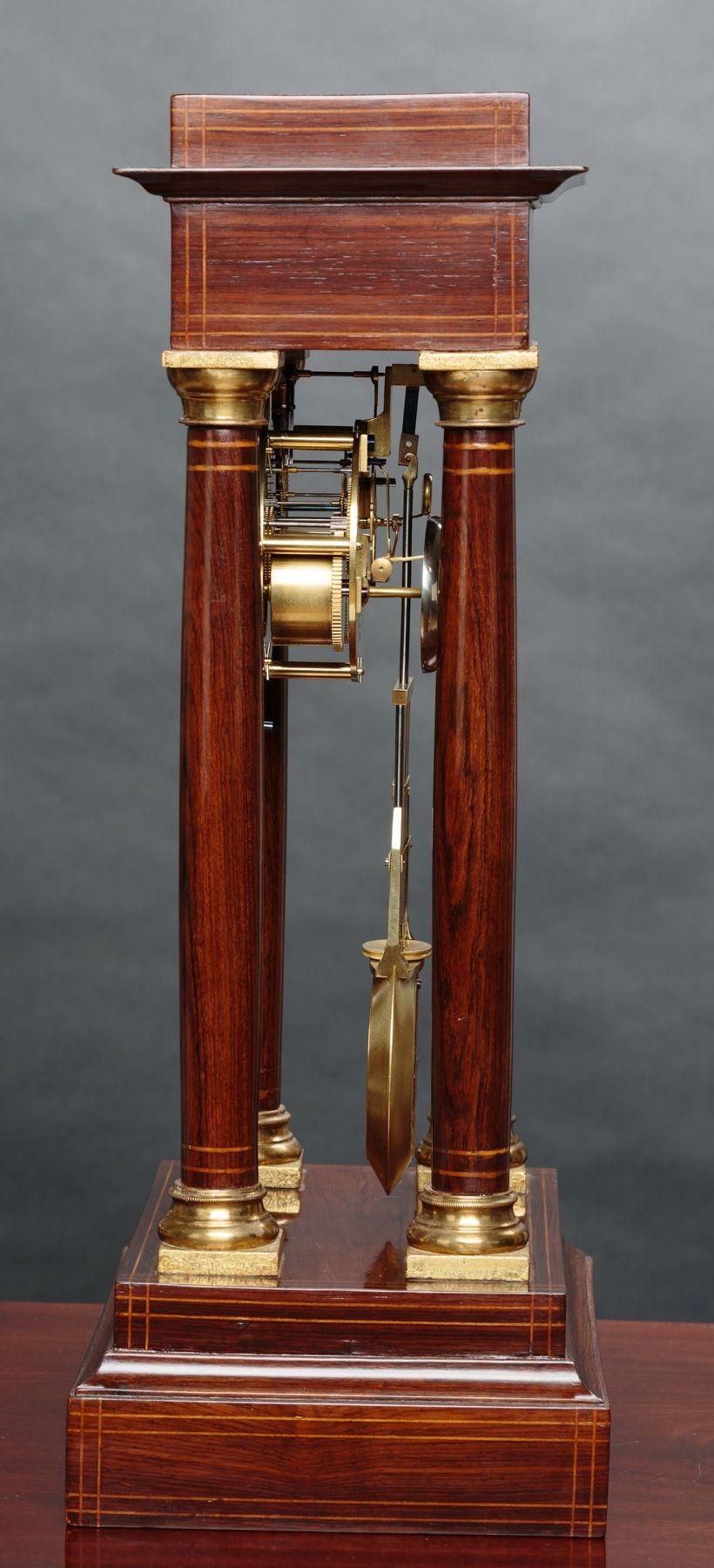 Rosewood Portico Regulator Mantel Clock

Housed in a fine quality Rosewood portico case with boxwood stringing, turned pillars with brass capitals, gilded cast foliate bezel and standing on an inlaid stepped base.
Silvered dial with Roman numerals,