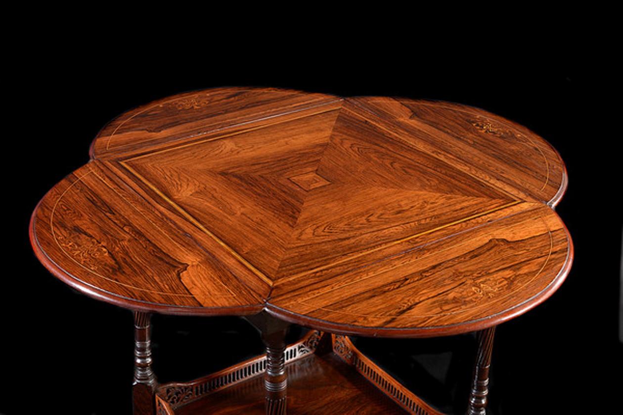 A fine quality rosewood and satinwood inlaid occasional table with four rounded drop flaps that can be raised to increase the size of the table top.

The whole supported on four turned, tapering and reeded legs that unite with a galleried platform