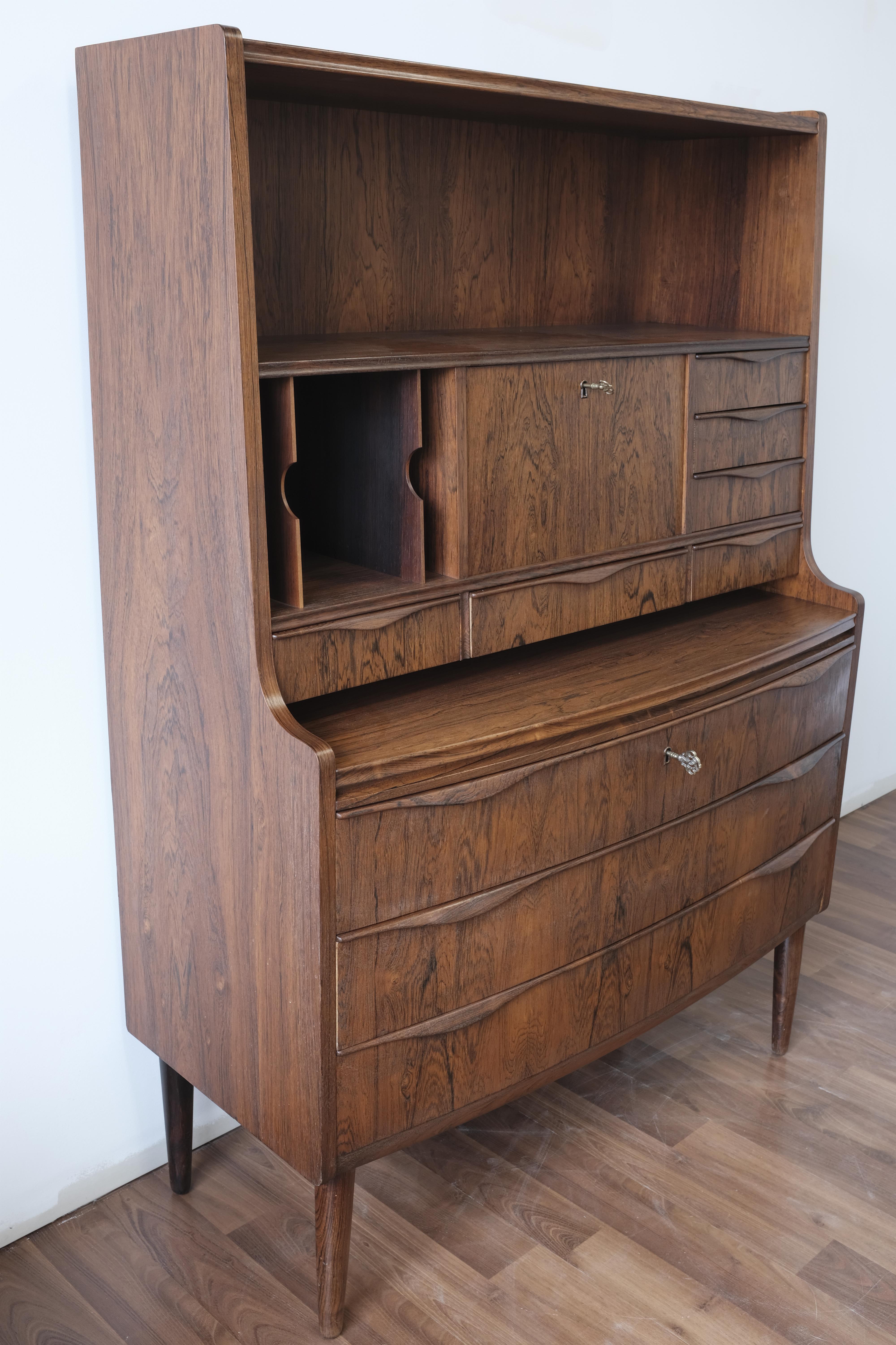 Rosewood secretary designed by Ib Kofod-Larsen and manufactured by A. Andersen & Bohm cabinetmakers.

The piece is constructed of solid wood with rosewood veneers, edging and drawer pulls, and features three lower drawers with a gentle outward