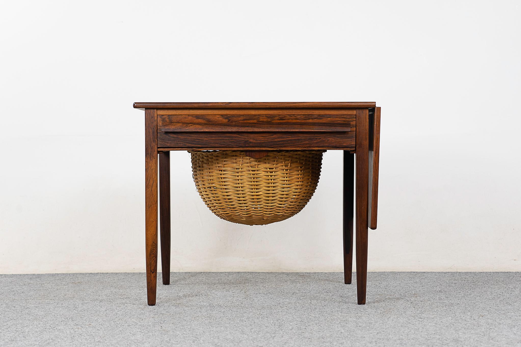 Rosewood sewing table by Johannes Andersen, circa 1960's. Sweet sewing table, can double as a perfect end table or accent piece. Handy drawer with fitted interior, original woven basket sides out for sleek storage.

Unrestored item, some marks