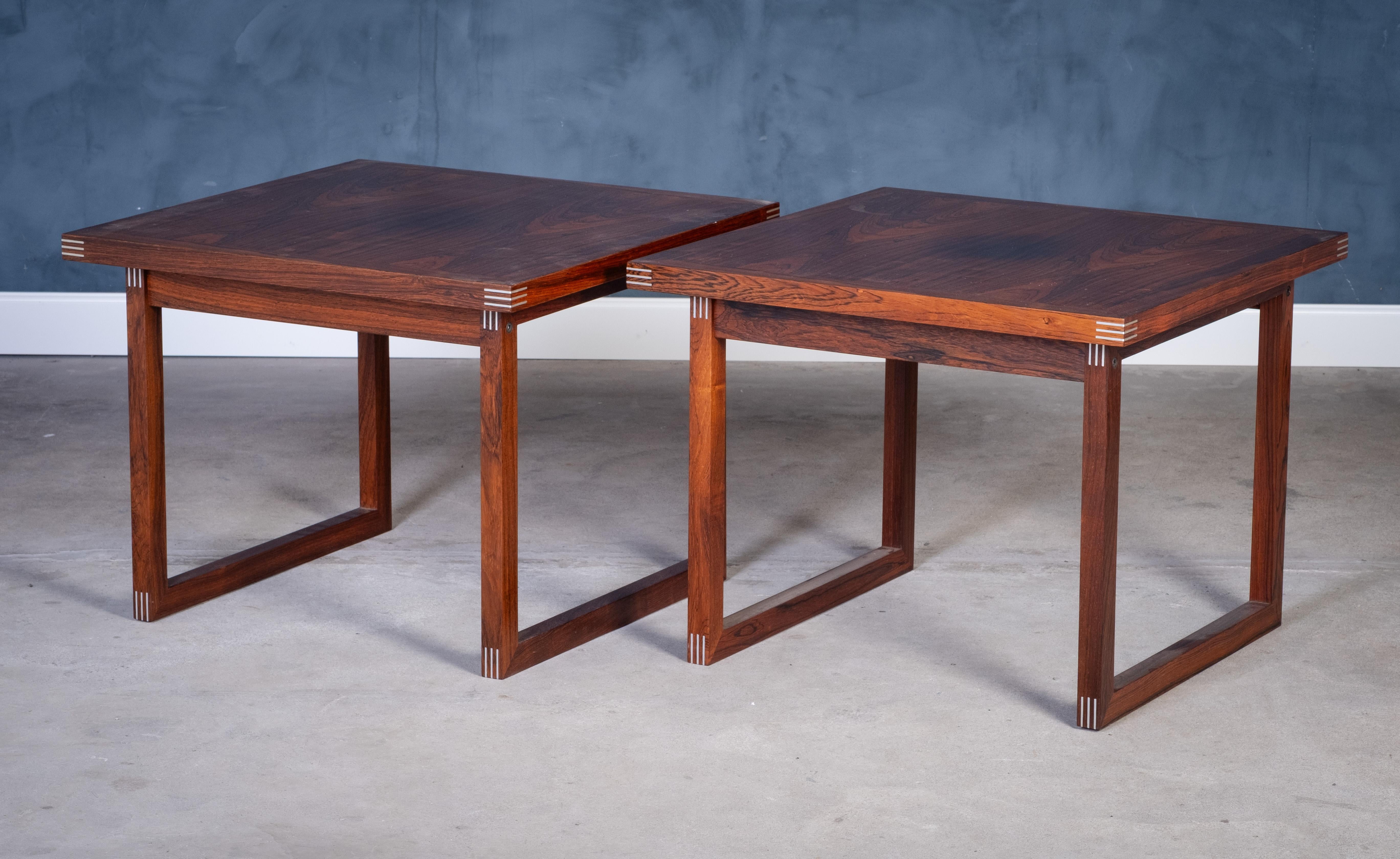 Pareja de mesas auxiliares diseñadas por Rud Thygesen y fabricadas por Heltborg Møbelfabrik en la década de 1960. Fabricadas en madera de palisandro ricamente veteada, estas mesas presentan las características juntas angulares del diseñador con tres