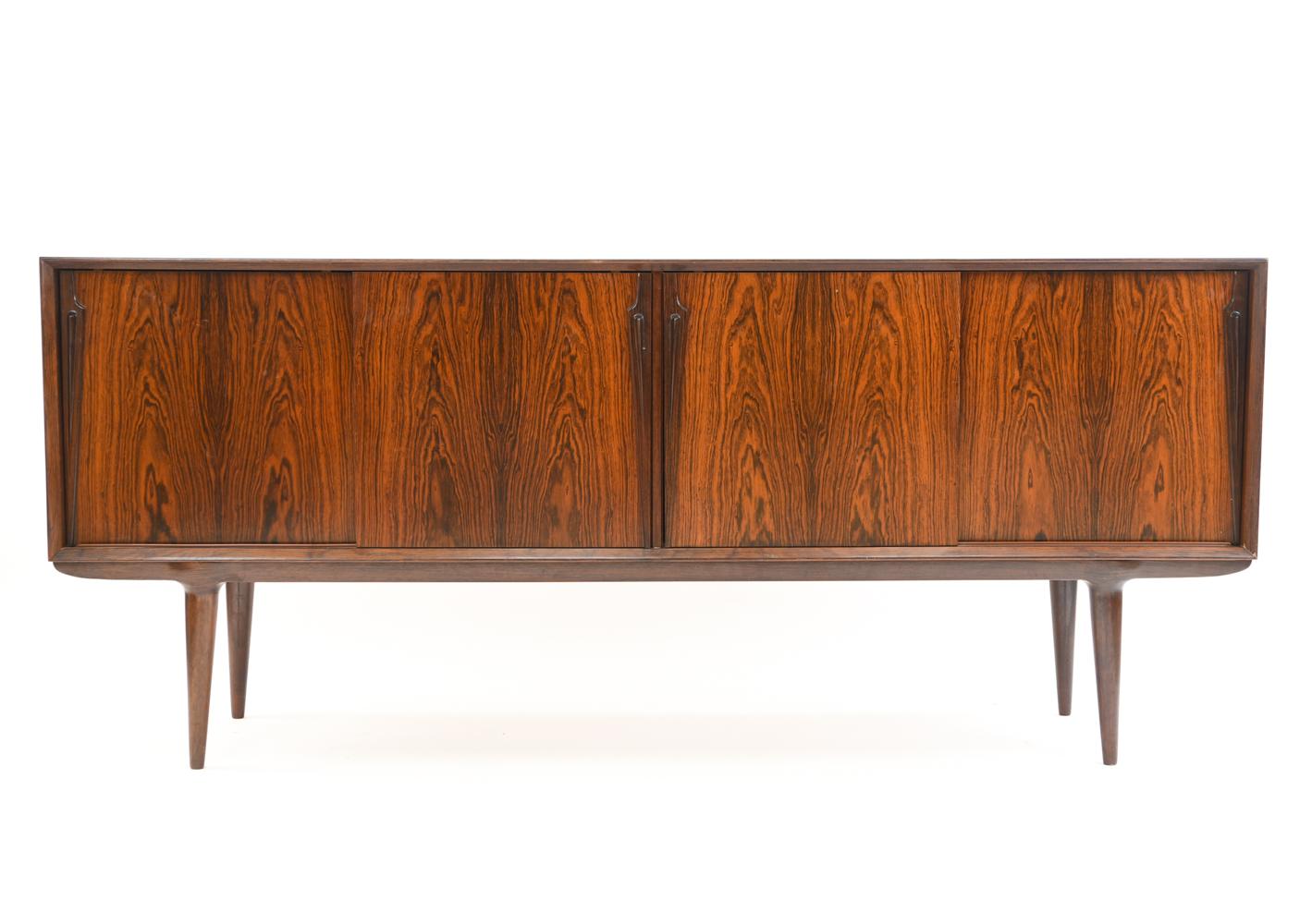 This gorgeous rosewood sideboard was designed by Gunni Omann for Omann Jr. The bevel-edged case sits on tapered legs and features four sliding doors with long organic handles. Inside are two adjustable shelves and, to the left, six felt-lined tray