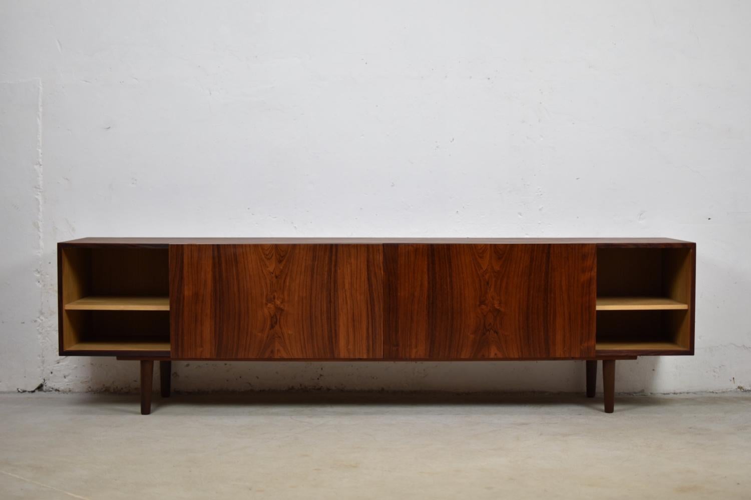 Stunning sideboard by Ib Kofod-Larsen for Faarup Mobelfabrik, Denmark 1960s. This lowboard is made out of rosewood and has a front with three sliding doors enclosing shelves and two pullout trays. Absolutely mint condition and an amazing grain on