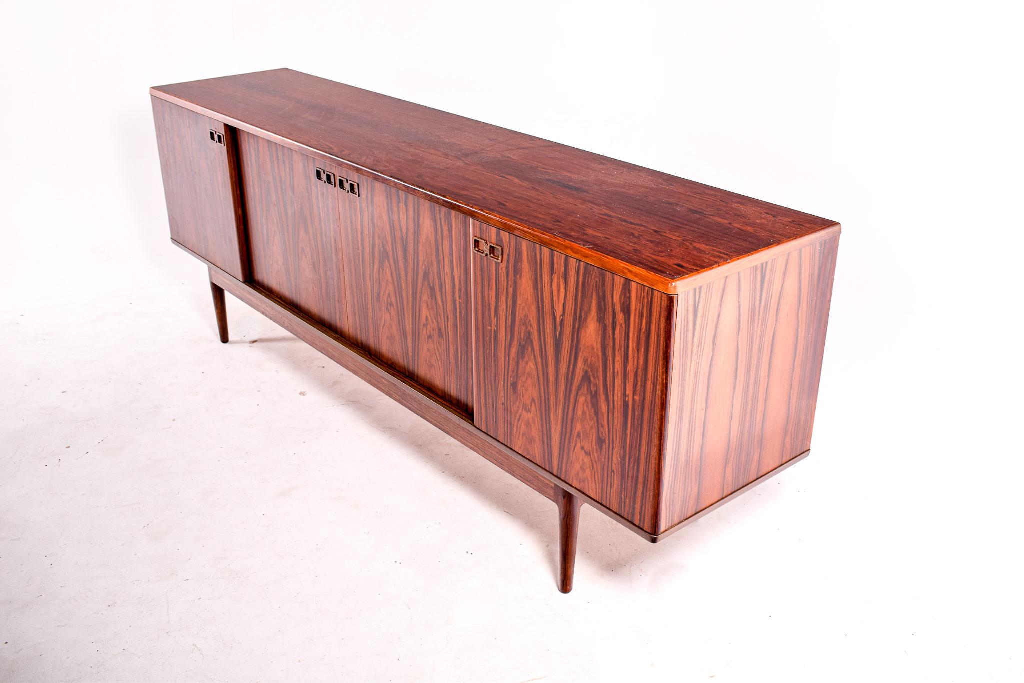 This beautiful sideboard in rosewood was designed by Johannes Andersen in the 1960s. Manufactured by Uldum Møbelfabrik. Consists of four sliding doors, adjustable shelves in height and interior cutlery drawers offering several possibilities of