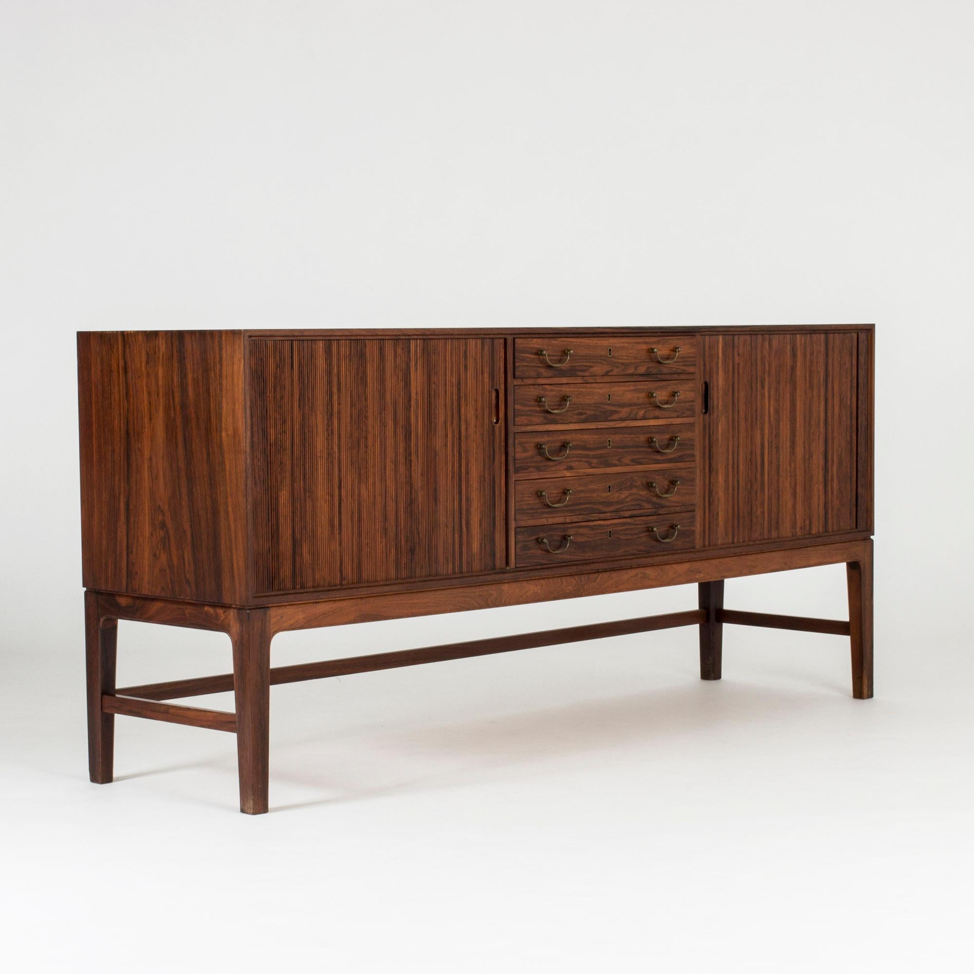 Elegant rosewood sideboard by Ole Wanscher, with a centred drawers with brass handles and jalousie doors on either side hiding shelves inside. Nice contrasting direction of the lines of the drawers and the jalousies lines.