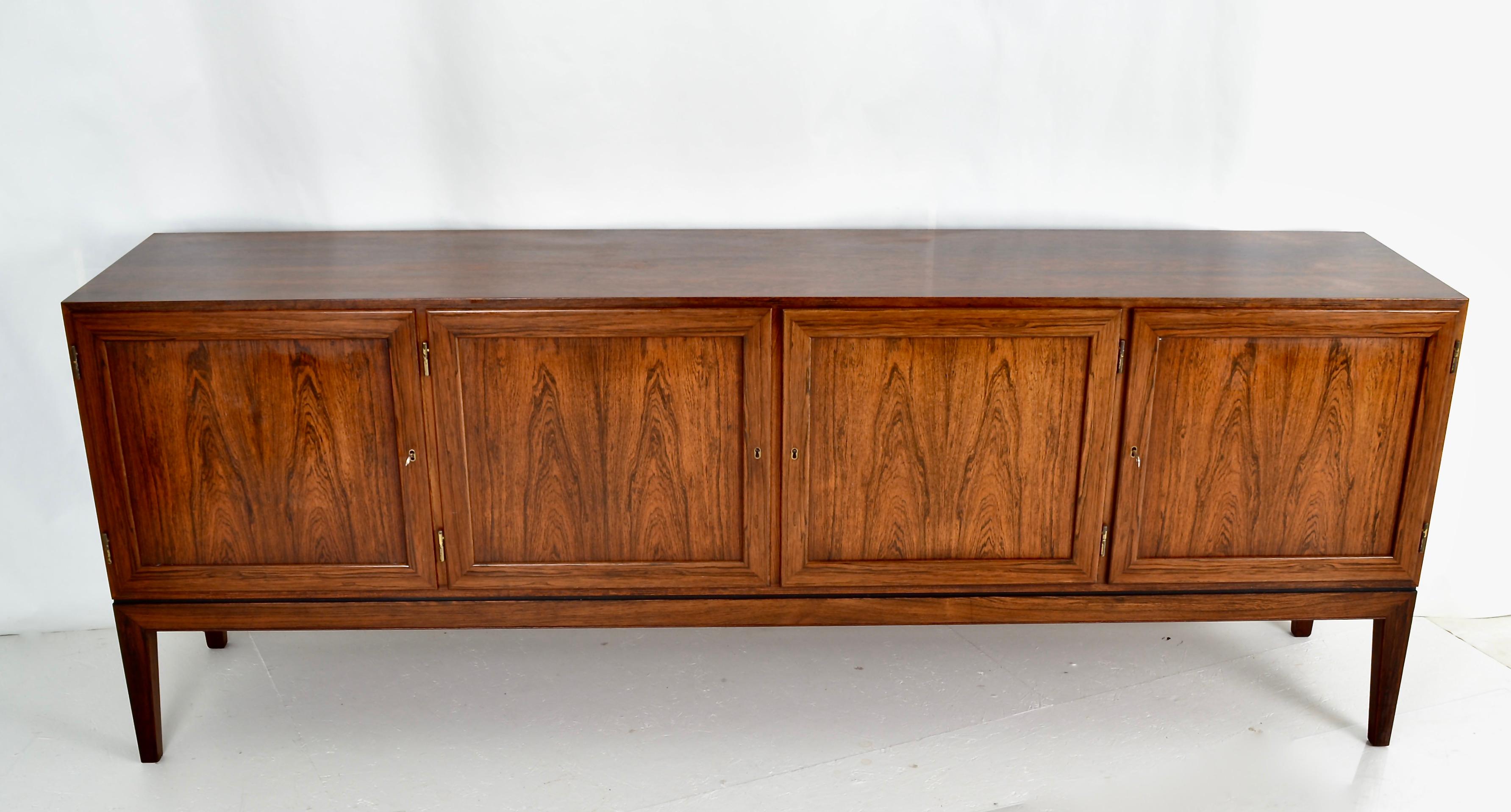 Figured rosewood with a rich finish makes this sideboard a stand-out. Classic Danish modern design with tapered legs and four paneled doors. Felt-lined silverware drawers on left. Shelves in center and right.