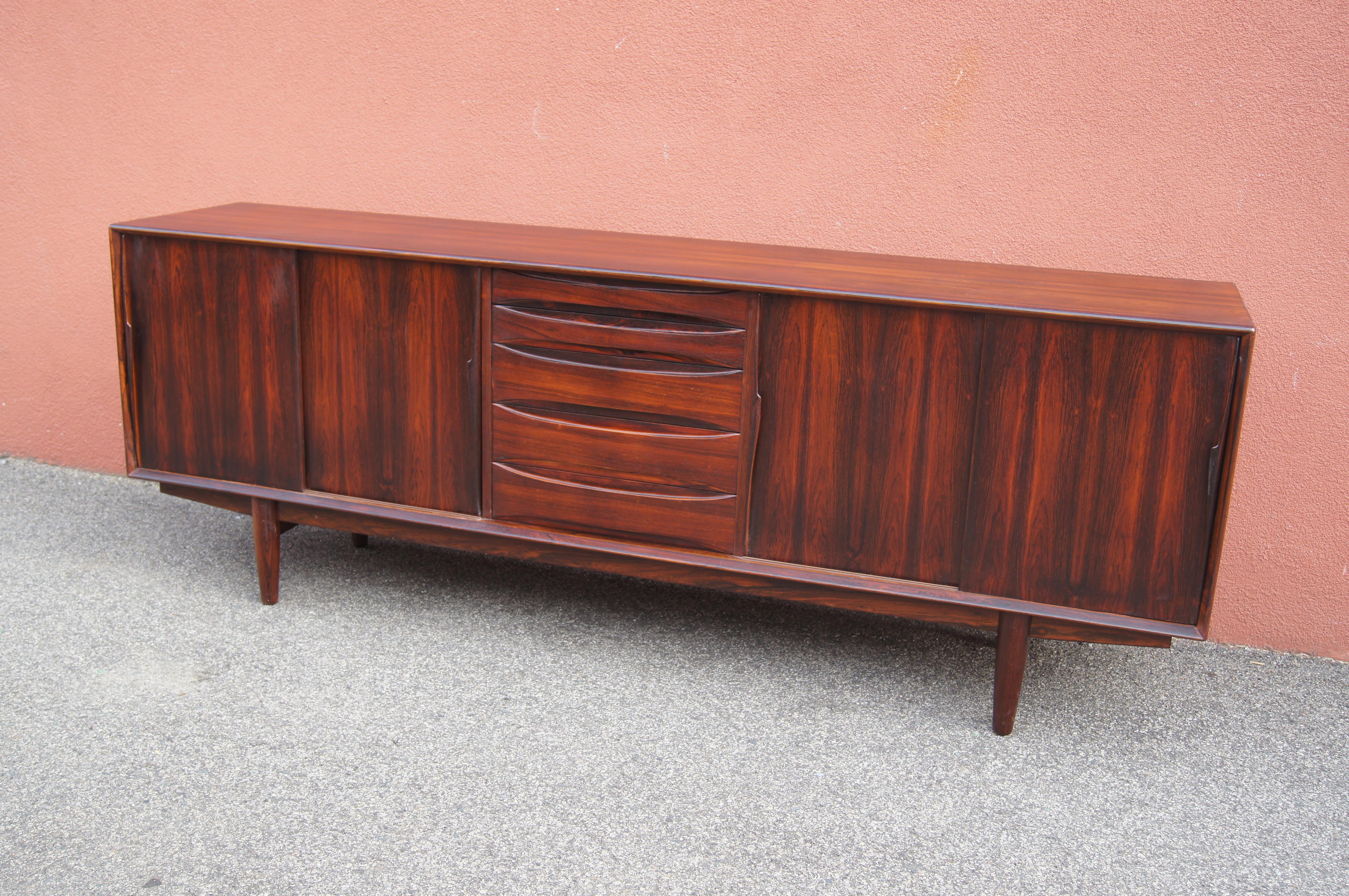 Designed by Arne Vodder for Skovby Møbelfabrik, this sideboard, model 7738, comprises a rosewood case on a plinth base. At center are five drawers, the top two of which are narrower than those below. On either side, two doors with elegant sculptural