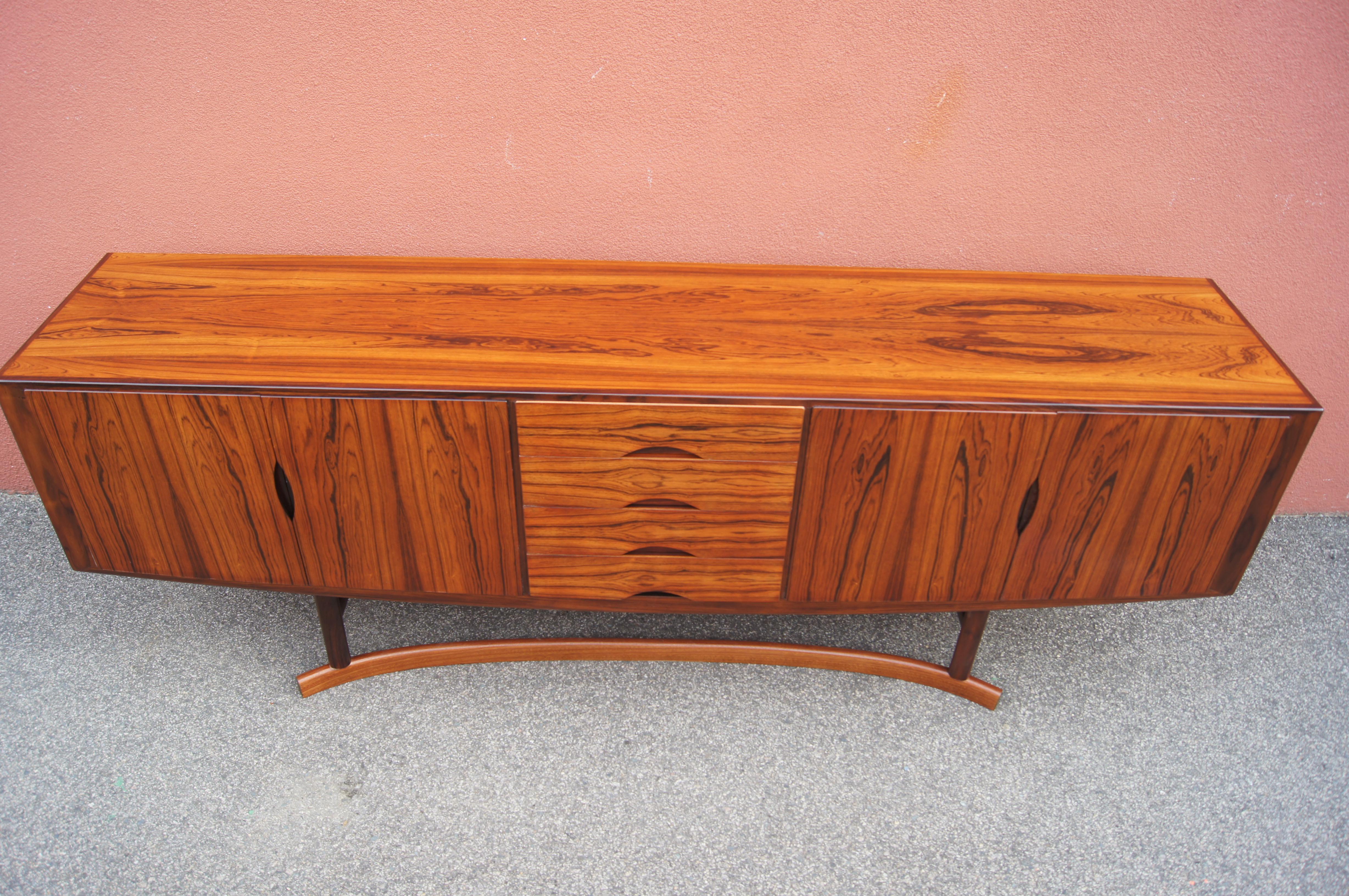 Johannes Andersen designed this extraordinary sideboard, model HB20, for Hans Bech. The finely crafted Brazilian rosewood case curves at bottom, echoed by the arced form of the base. At center are four drawers with curved inset pulls. The doors to