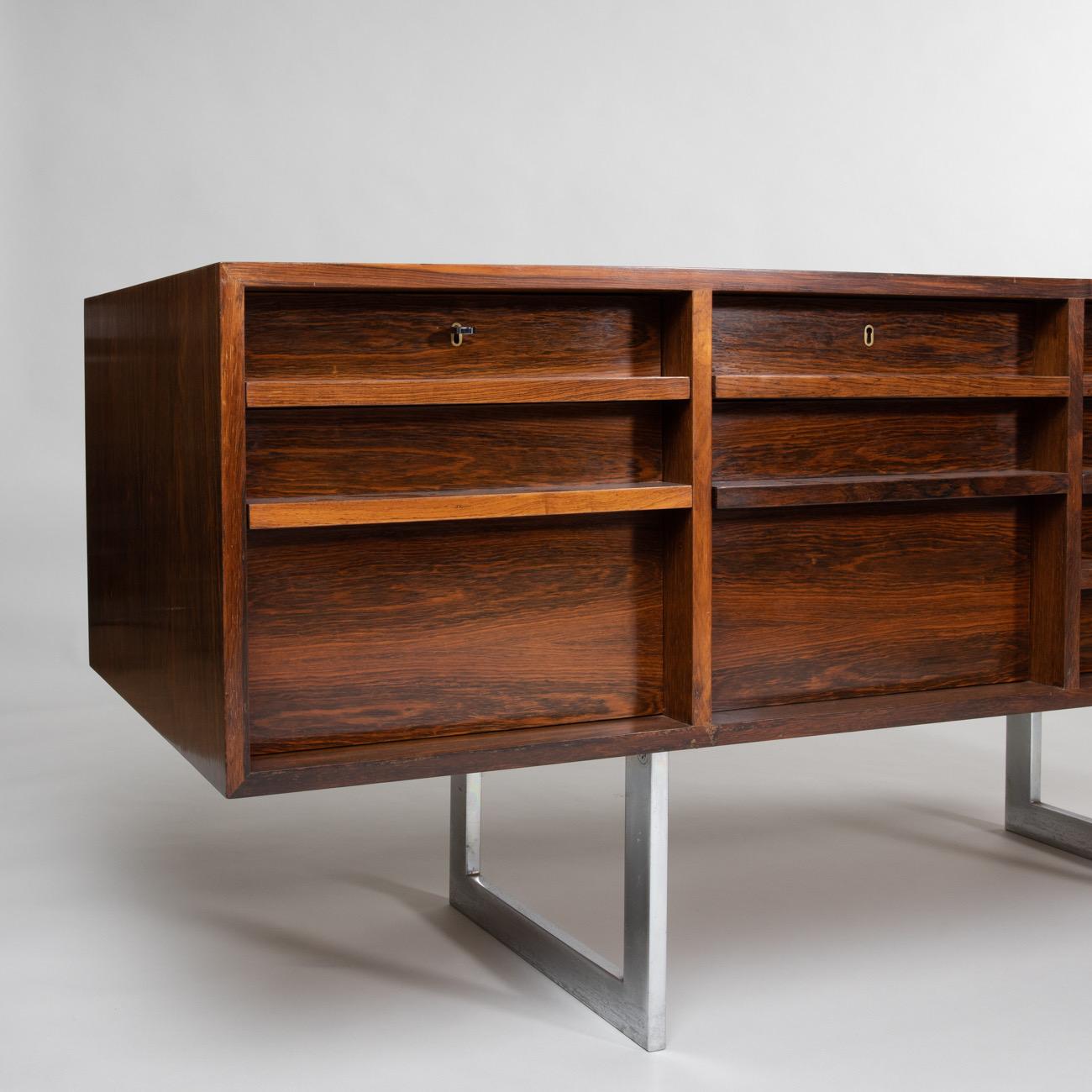 Sideboard resting on chrome legs, also called Credenza.
Designed by Bodil Kjaer in the early 1960s, this piece of furniture is part of the same series as the iconic desk complement found in several James Bond films.
From Russia with Love;
You