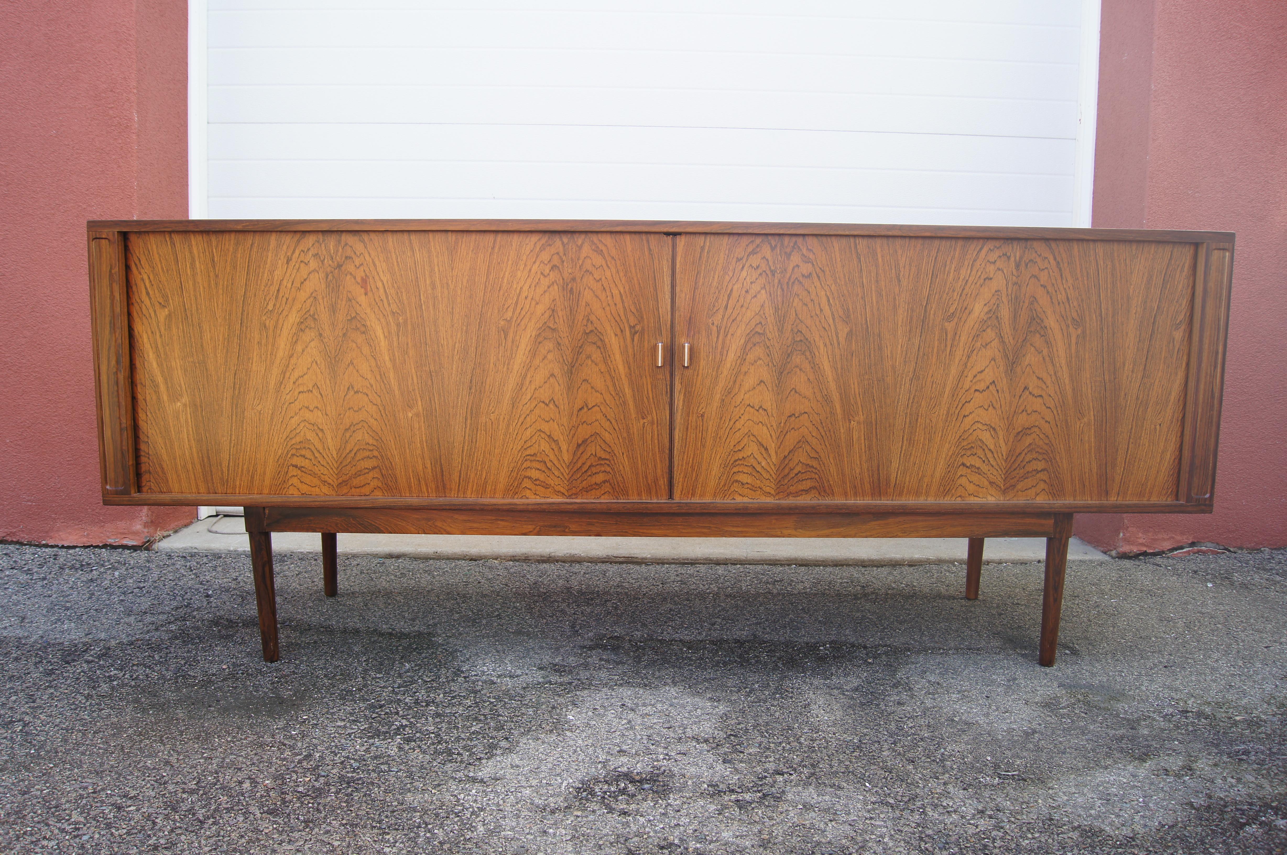 This hard-to-come-by mid-century sideboard was designed Peter Løvig Nielsen for Løvig Dansk. The rosewood frame has book-matched tambour doors that open with minimal pulls. Inside adjustable shelves — one on the left and two on the right — flank