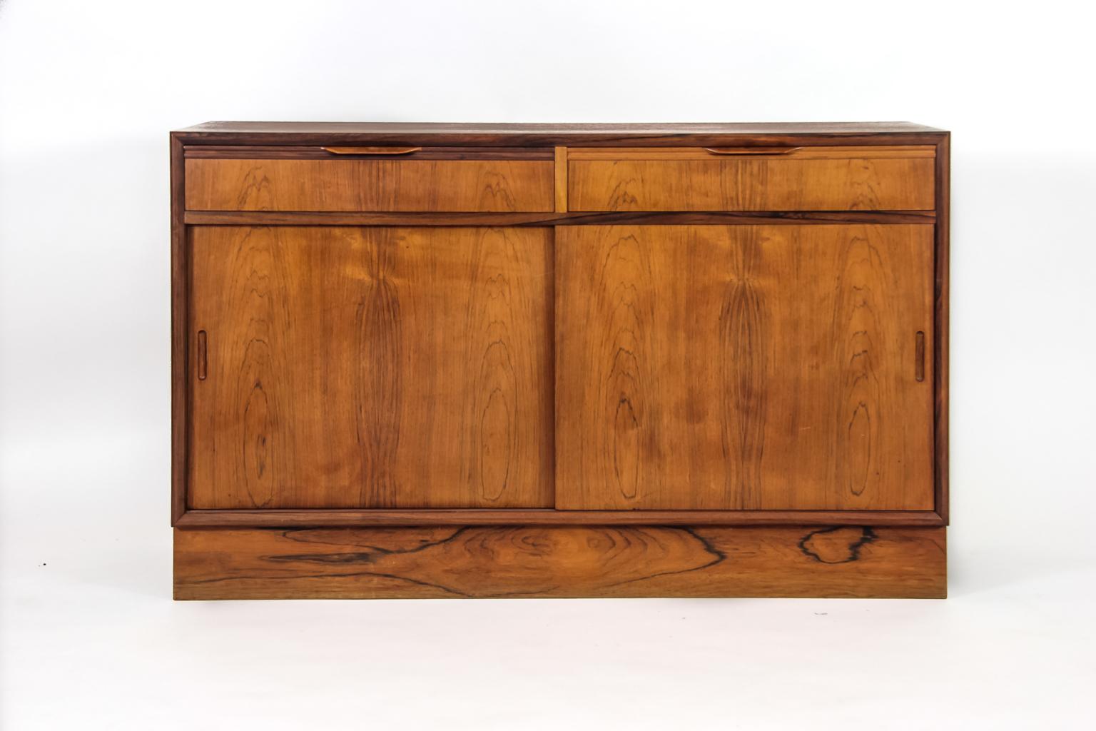 A sophisticated Danish 1960s rosewood cabinet with two drawer under top, long well-figured top above two drawers and two slide doors all in a rich match-booked Brazilian rosewood veneer with solid rosewood moulded handles and front frame, a good