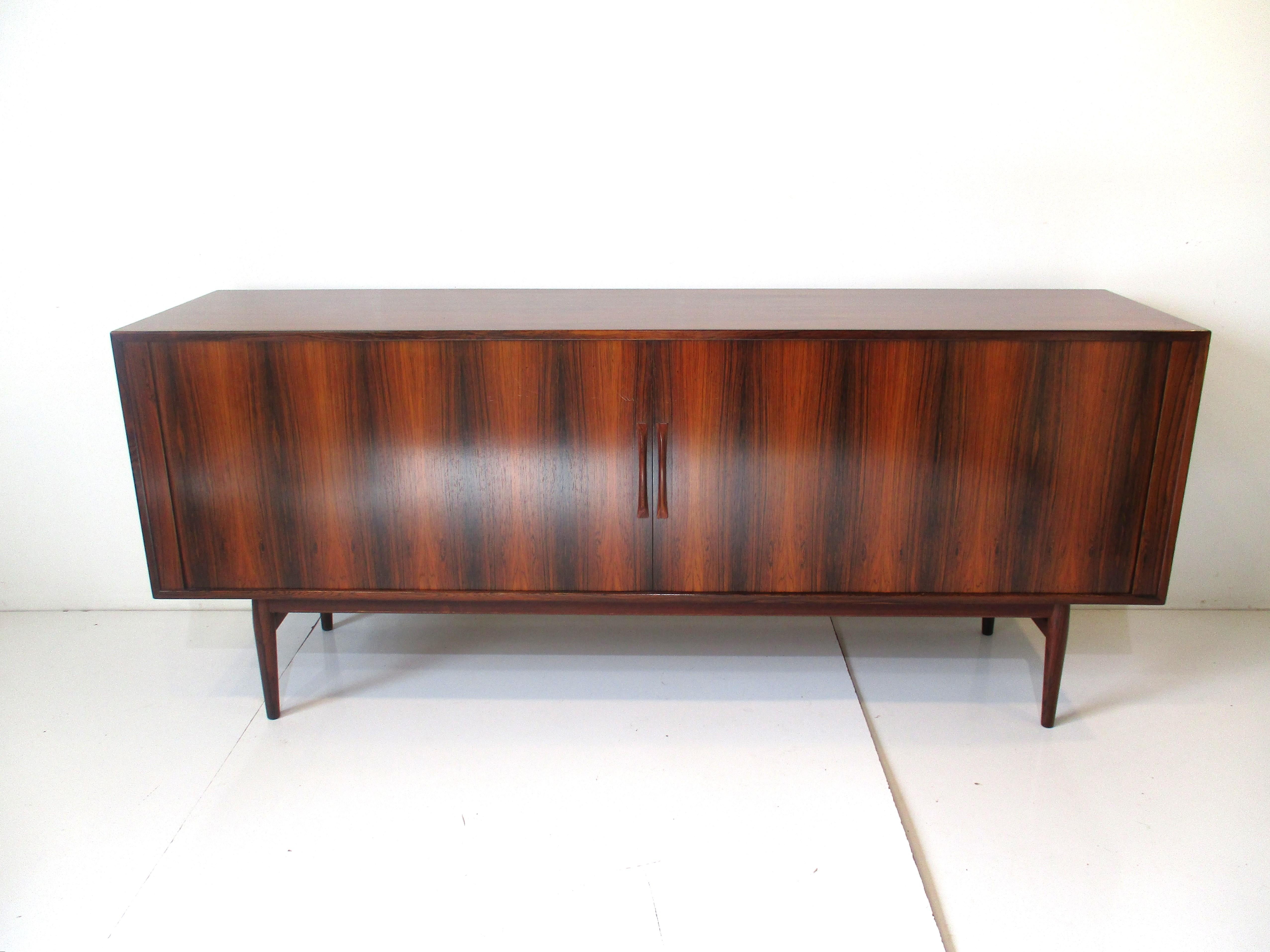 A very well crafted and designed Brazilian rosewood credenza / sideboard with wonderful book matched grained tambour door front . Ajustable shelves to the left, right and center of the piece with two small drawers to the middle section giving you