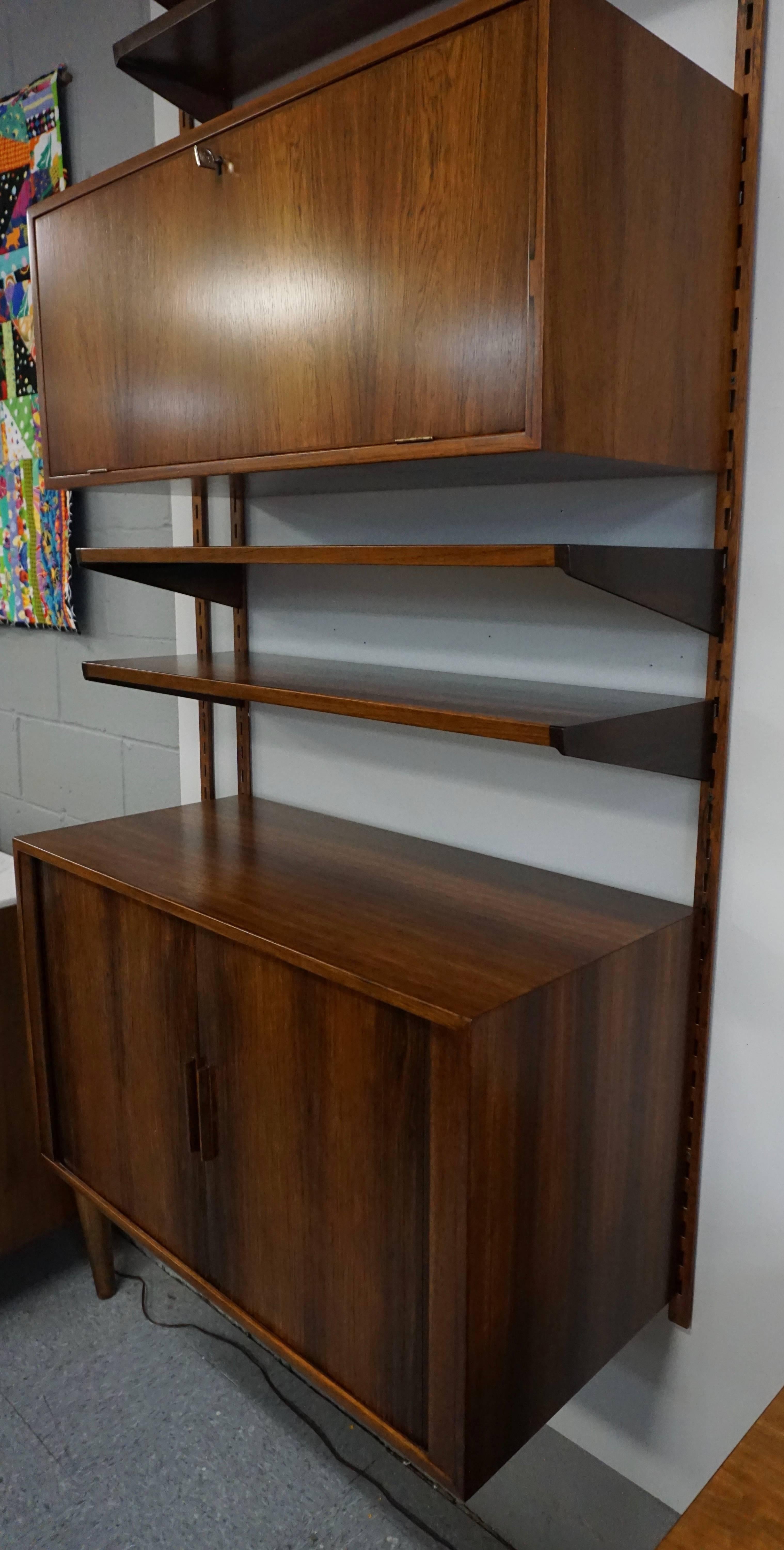 This rosewood wall mount system has four, shelves that measure: 7 D x 34 W, two shelves: 11 D x 34 W, one-bar cabinet 12.5 D x 34 W x 14 H and a tambour door cabinet, 15.75 D x 34 W x 19.5 H. The system has been lightly restored and is in very nice