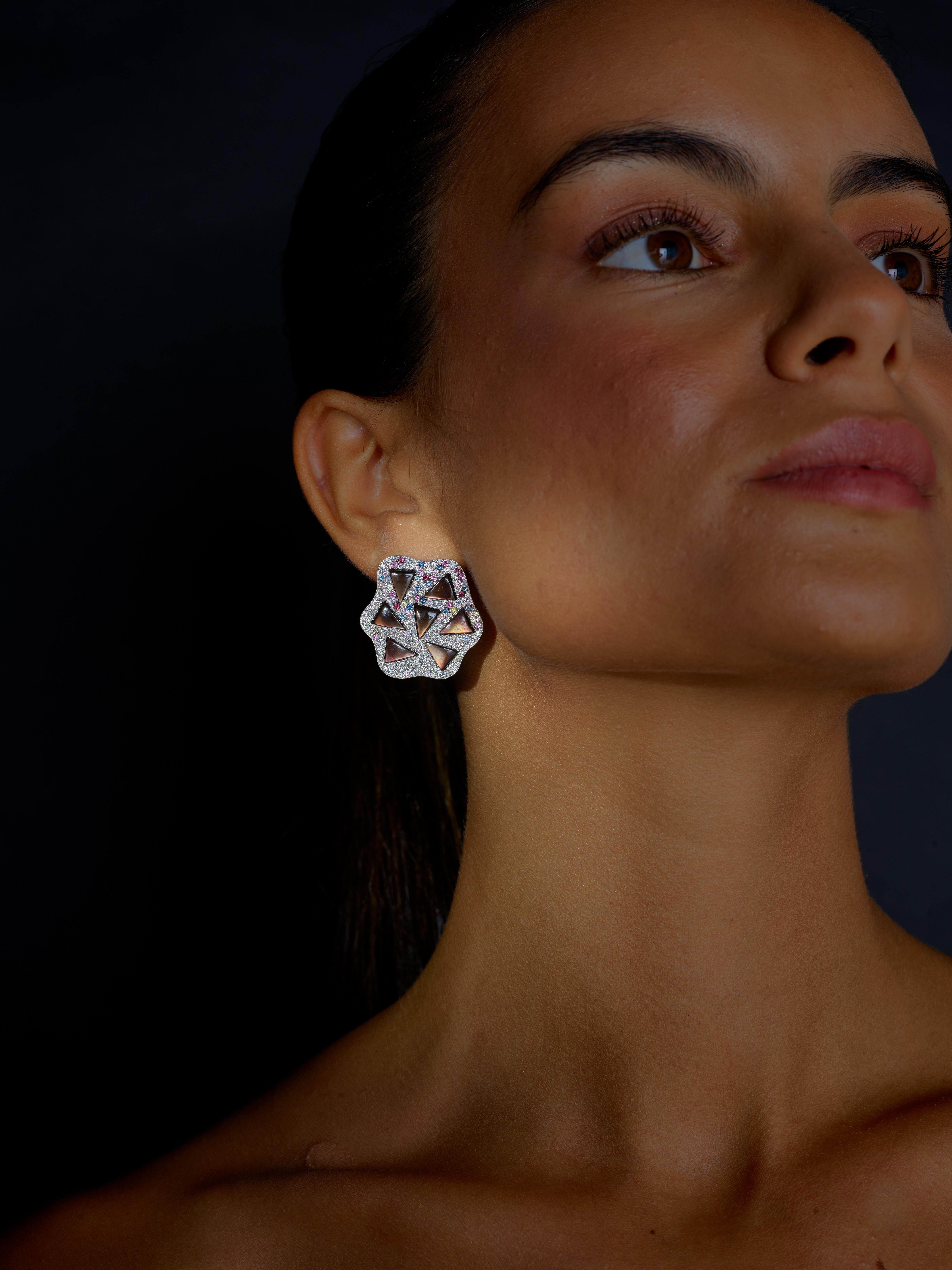 Creazione unica della casa portoghese Rosior, questi orecchini sono incastonati in oro bianco a 19,2 carati:
- 14 pezzi triangolari di Madreperla Nera, con sfumature di marrone, del peso di 8,05 ct;
- 428 zaffiri multicolore del peso di 4,26