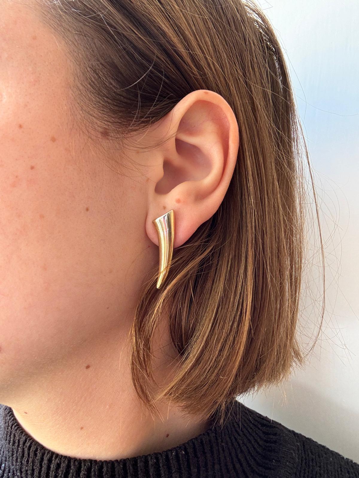 Orecchini a lobo in oro giallo 14k di Rossella Ugolini. Misurano 3 cm di lunghezza e 8 mm di larghezza e sono realizzati a mano in modo speculare a destra e a sinistra. La loro forma lineare e scultorea evoca un senso di forza.
Eleganza minimalista