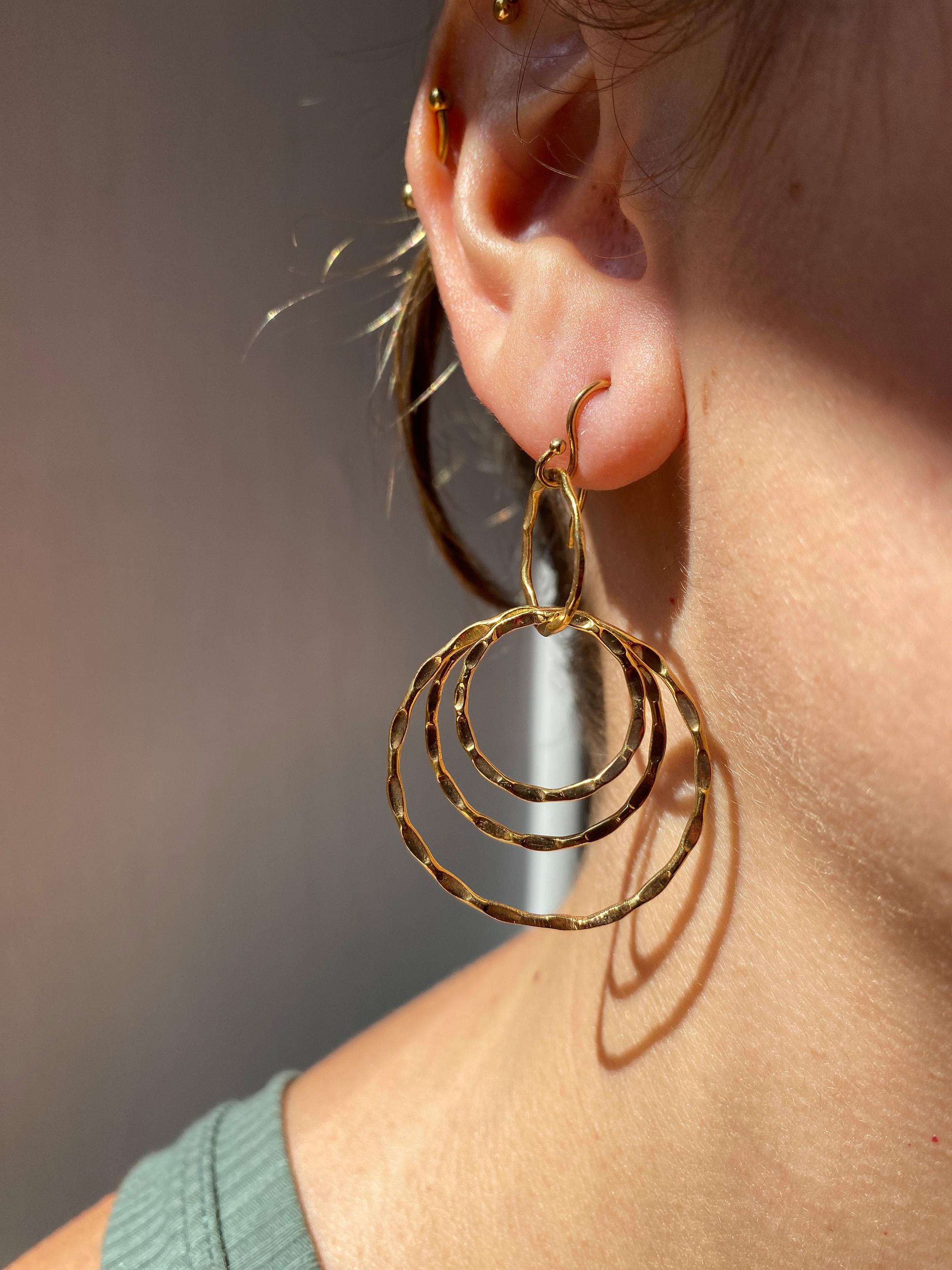 Introducing the Rossella Ugolini Dangle Drop Circle Earrings an 18K Yellow Gold masterpiece. Each circle is meticulously handcrafted and uniquely hammered, creating a captivating interplay of light. The design features a suspended hook on the lobe,