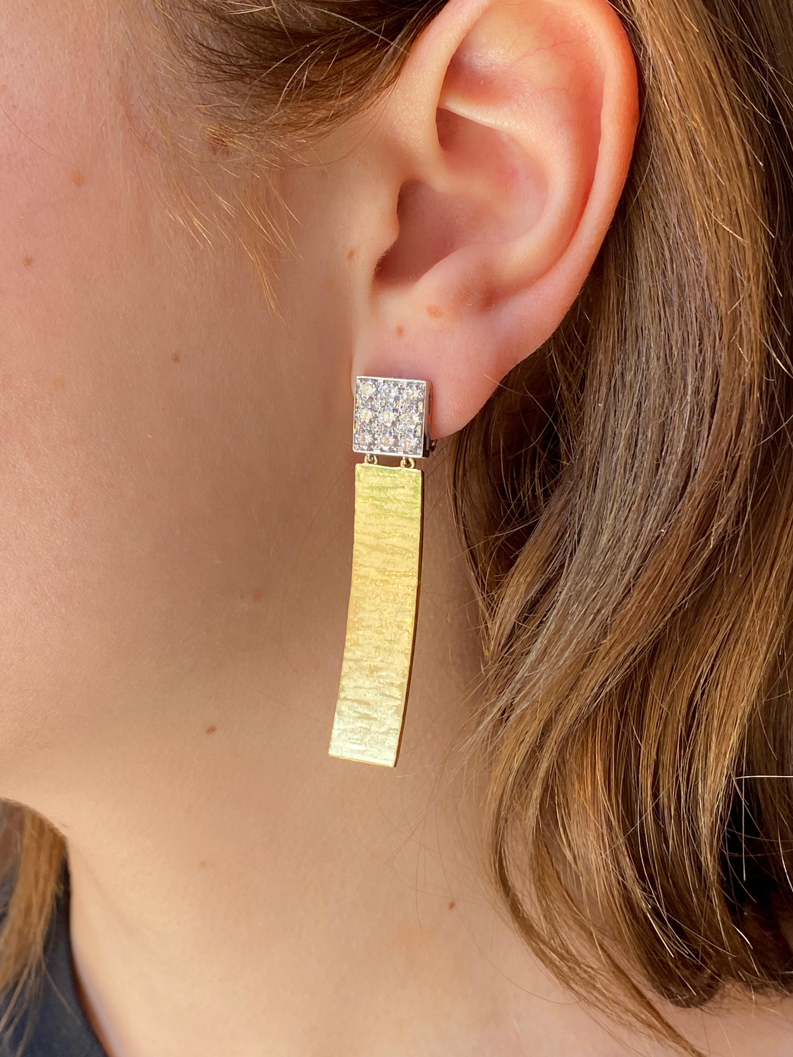 Gli orecchini Rossella Ugolini in oro giallo 18 carati martellato e graffiato con 1,80 carati di diamanti bianchi sono uno splendido esempio di eleganza contemporanea. Questi orecchini lineari, semplici ma preziosi, presentano una forma quadrata in