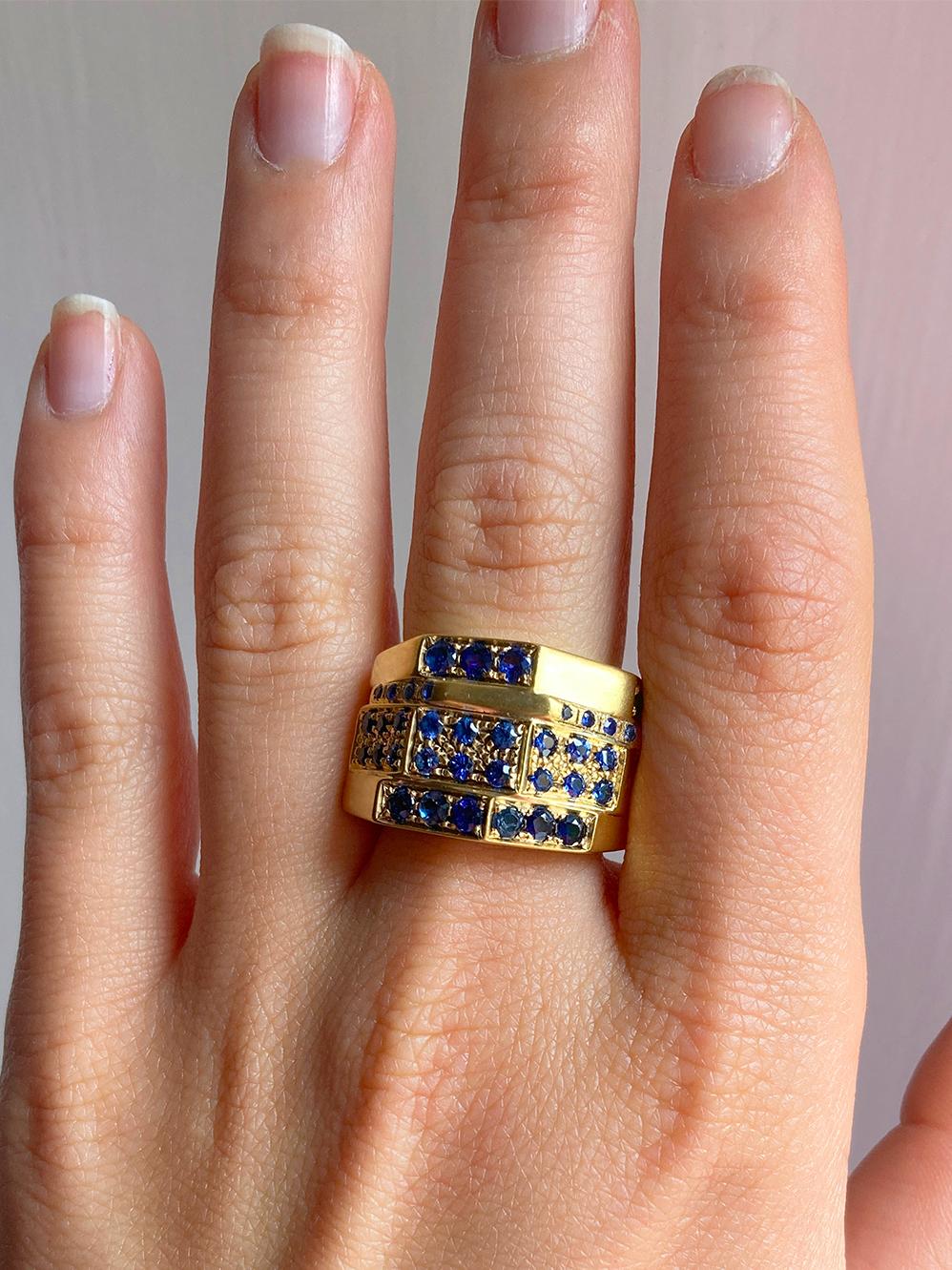 The Rossella Ugolini man band ring, crafted in 18k yellow gold and adorned with 9 carats of blue sapphires, is a striking piece from the Castle of Italy Collection. Weighing 15 grams and standing at a height of 0.31 inches (1.4 cm), this design