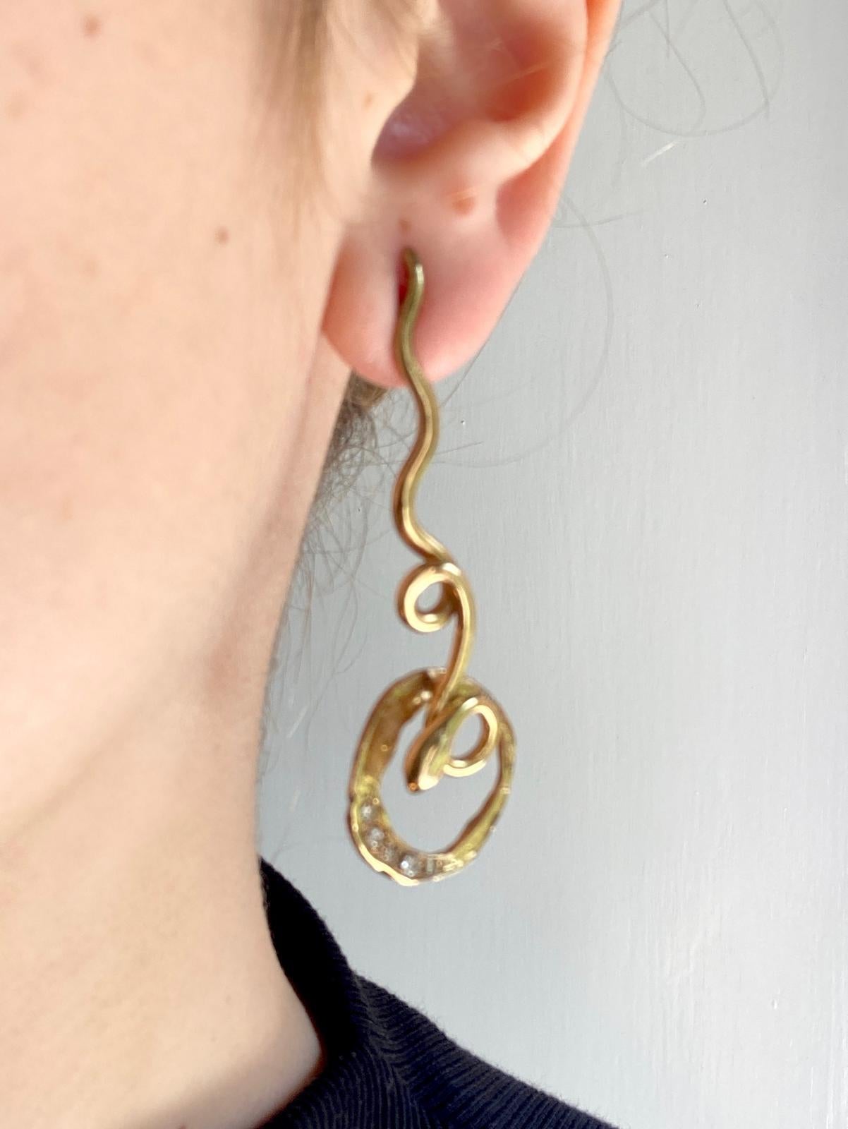 Rossella Ugolini Handcrafted Dangle Snake Earrings, a stunning blend of elegance and symbolism. These exquisite earrings, crafted in 18 karat yellow gold, feature 0.20 karats of grey diamonds. Their circular shape and fluid, intertwined lines create