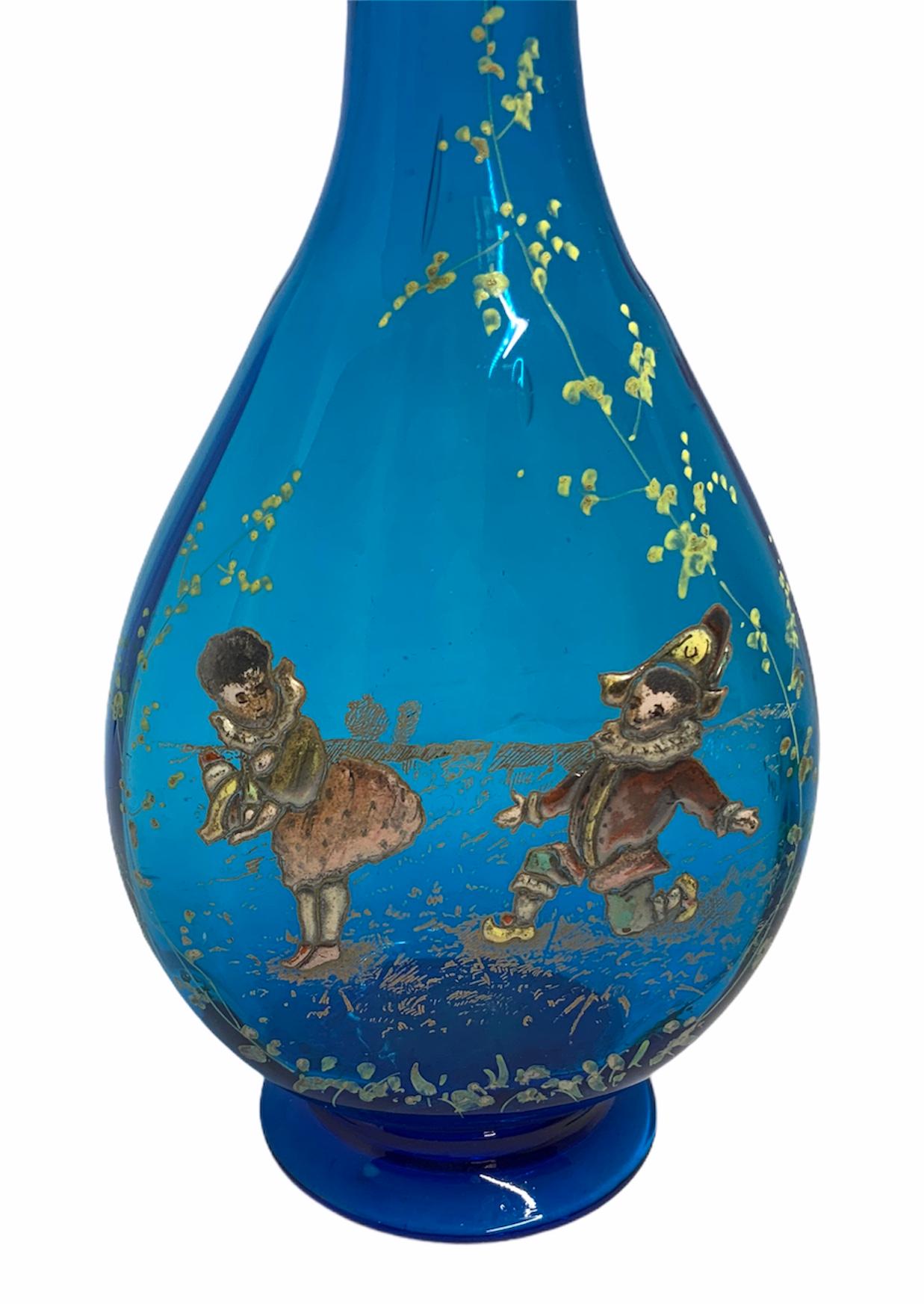 This is a royal blue glass decanter depicting a gold- silver enamel painting of a girl & an harlequin. Behind them, there is also some gilt stenciled decor of what appears to be a lake or pond. The rim of the bottle is shaped as a ruffle and the