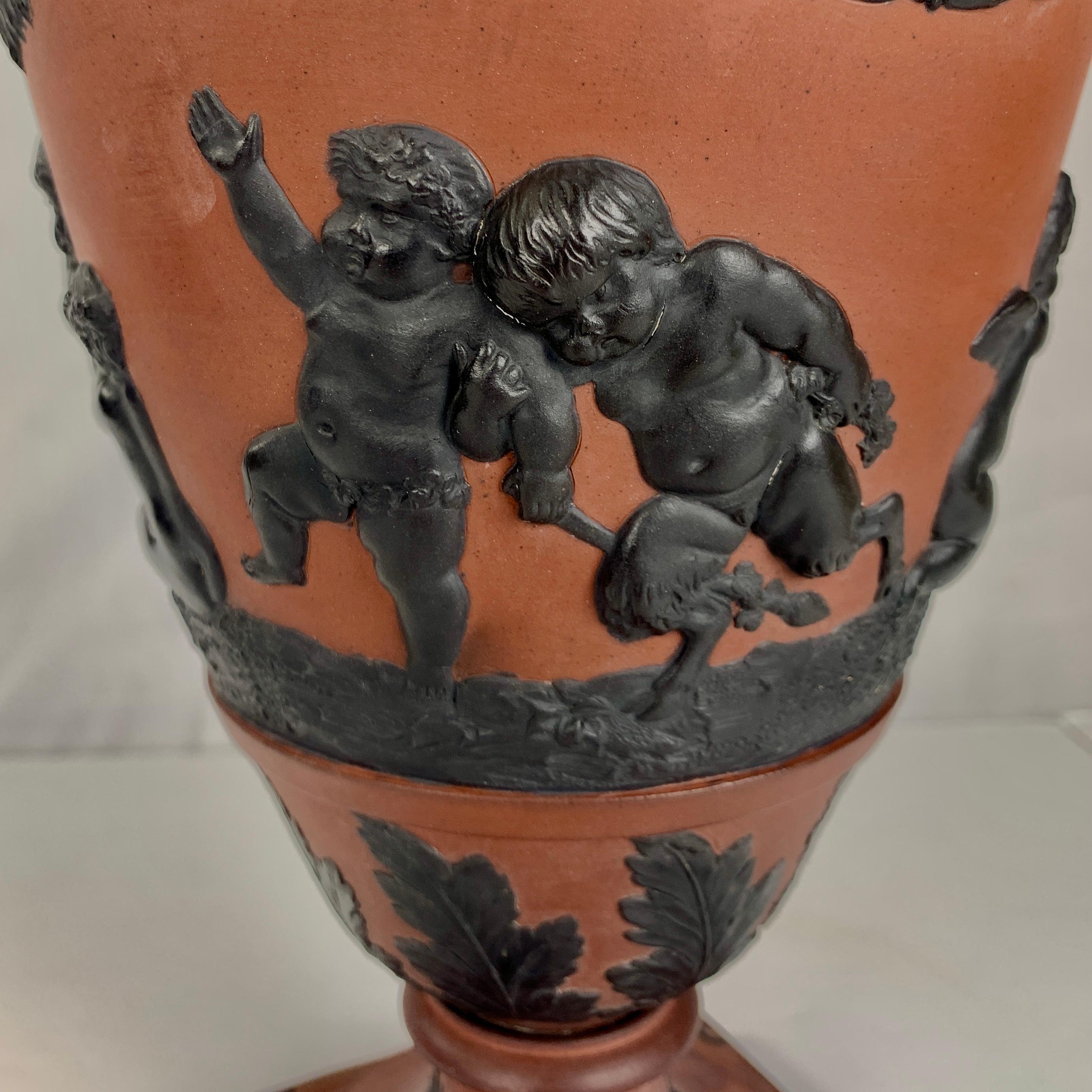 This magnificent vase, made in England circa 1815, is a true work of art. Crafted from luxurious Rosso Antico stoneware and adorned with applied black basalt in deep relief, this vase exudes elegance and excitement.
The Bacchanalian and celebratory