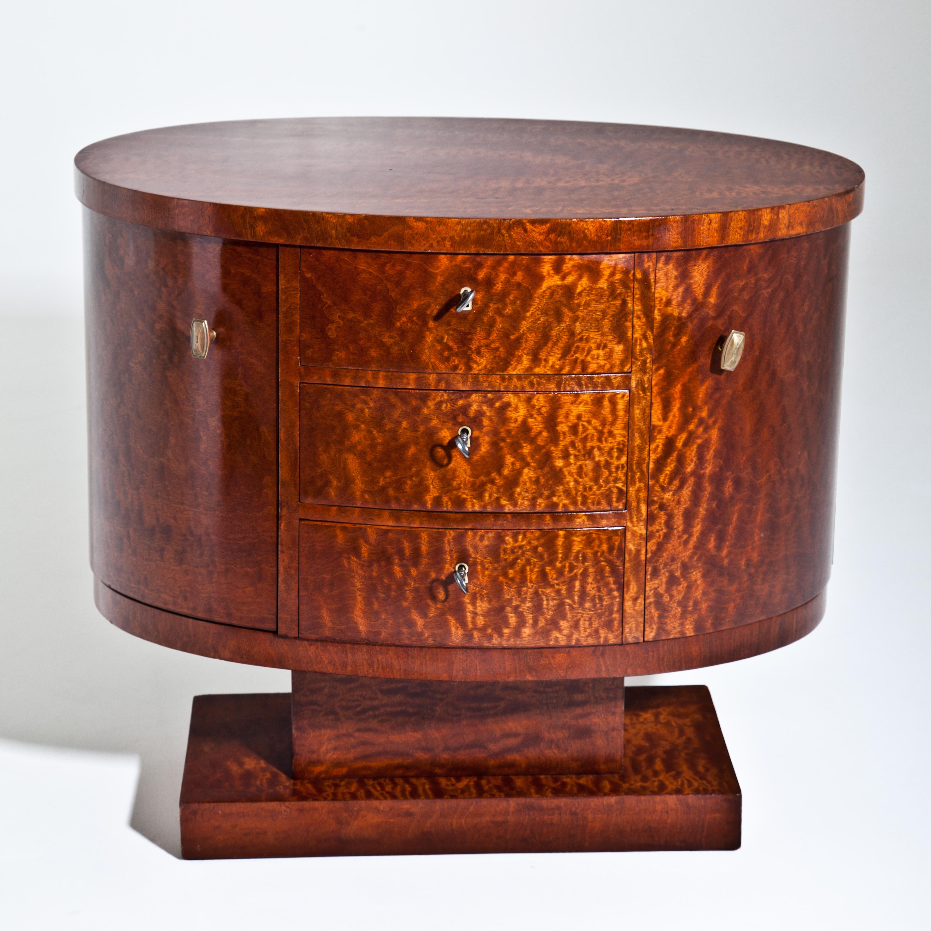 Small Art Deco sideboard or nightstand veneered in thuja wood. The oval corpus with three drawers and two doors is mounted on a rotating base.