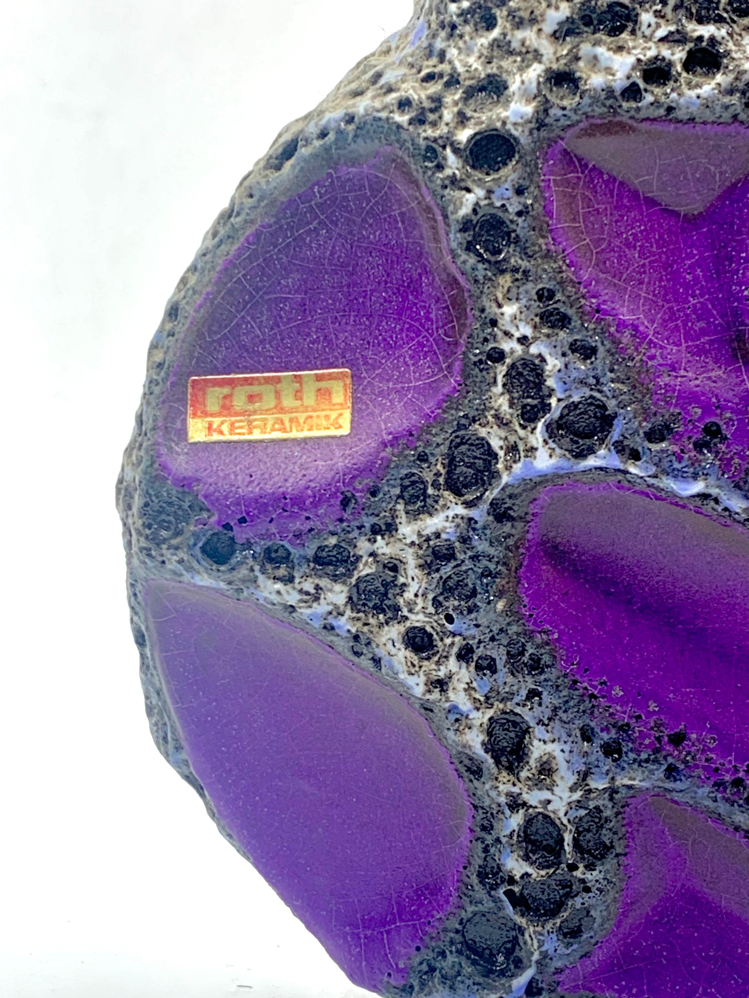Eine seltene violett getäfelte Vase mit zwei Henkelringen von Roth Keramik mit weißer und schwarzer Lavaglasur und blauer Umrandung, Musternummer 313.
Violett ist die einzige Farbvariante mit den weißen, lavaglasierten Rändern.
Diese Form gab es in