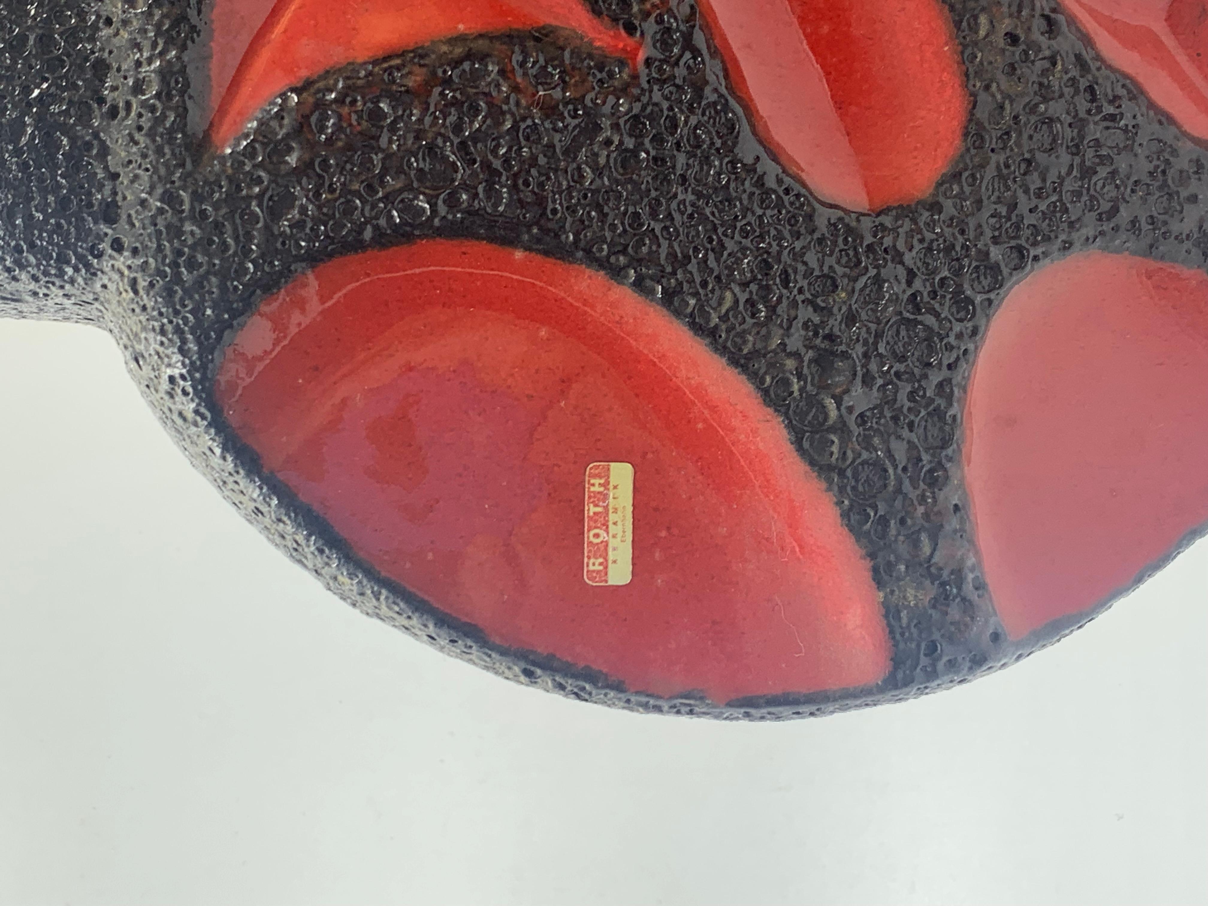 Jarrón Roth Keramik con 2 asas anulares. Esmalte de lava negra y motivo ovalado rojo brillante moldeado. La forma, numerada 314, se encuentra en 2 tamaños, siendo éste el mayor con 41 cm.
Como ocurre con la mayoría de los jarrones de Alemania