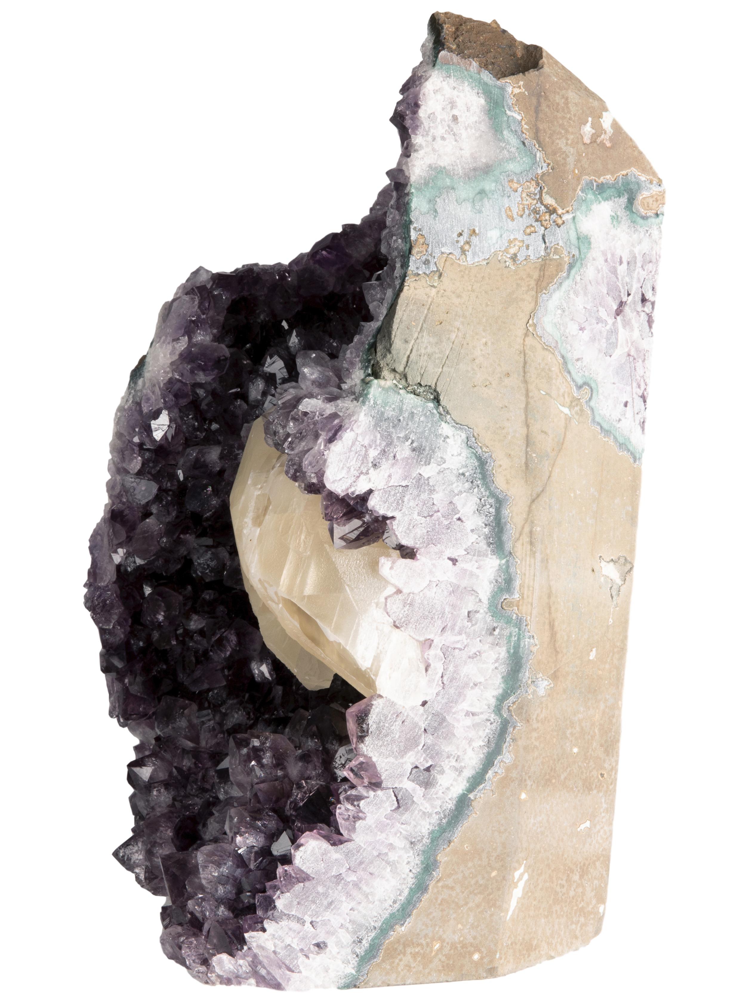 In this piece, the rough amethyst's rich purple colouration is brilliantly pierced by the matt cream calcite formation that is bordered by a green celadonite and white quartz in a manner typical of Uruguayan crystal formations, but atypical of most