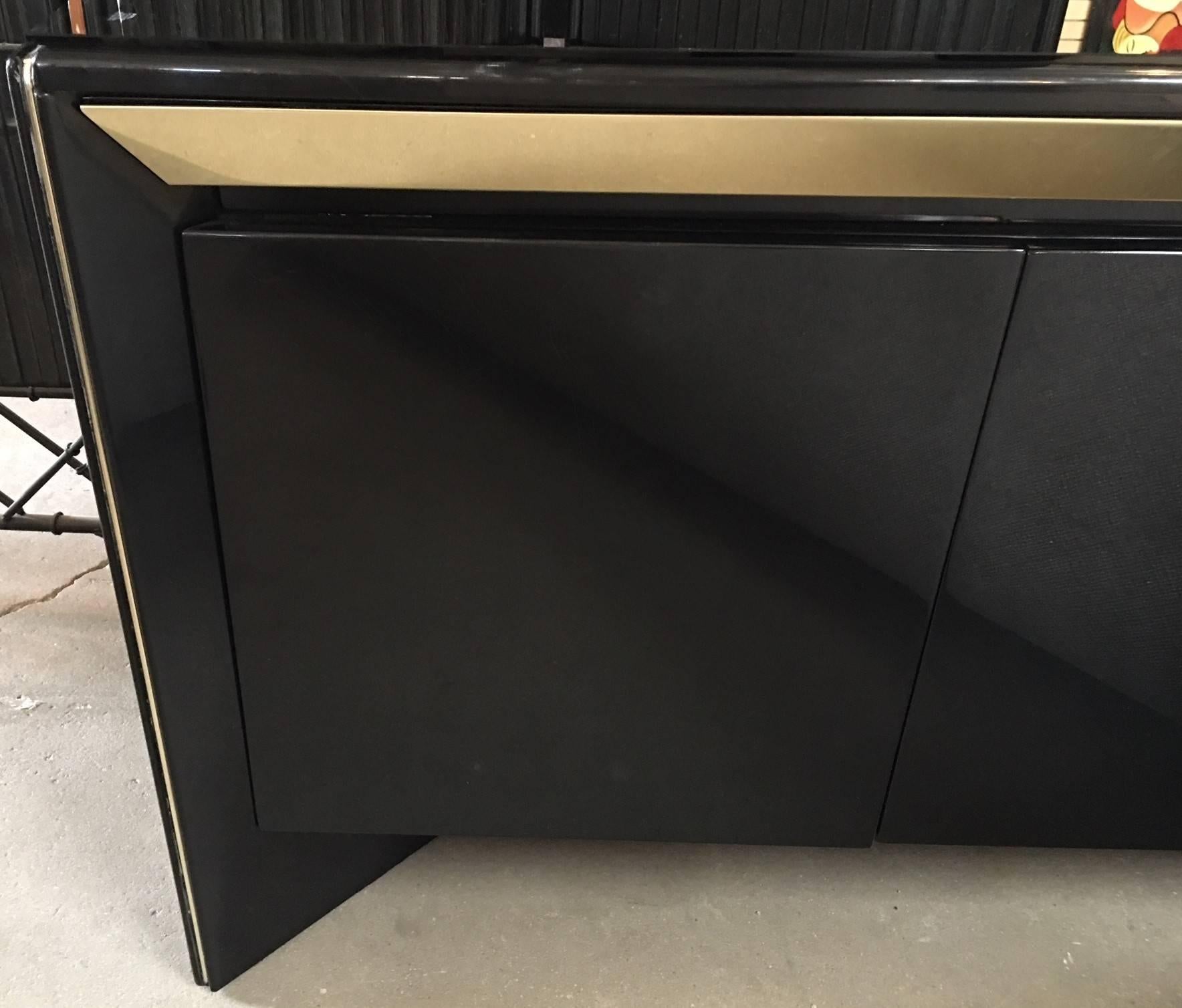 Stunning black lacquer credenza with four push-latch doors and brass trim. The base is recessed and the top has a piece of glass protecting the lacquer.
The original matching table is available. See listing.