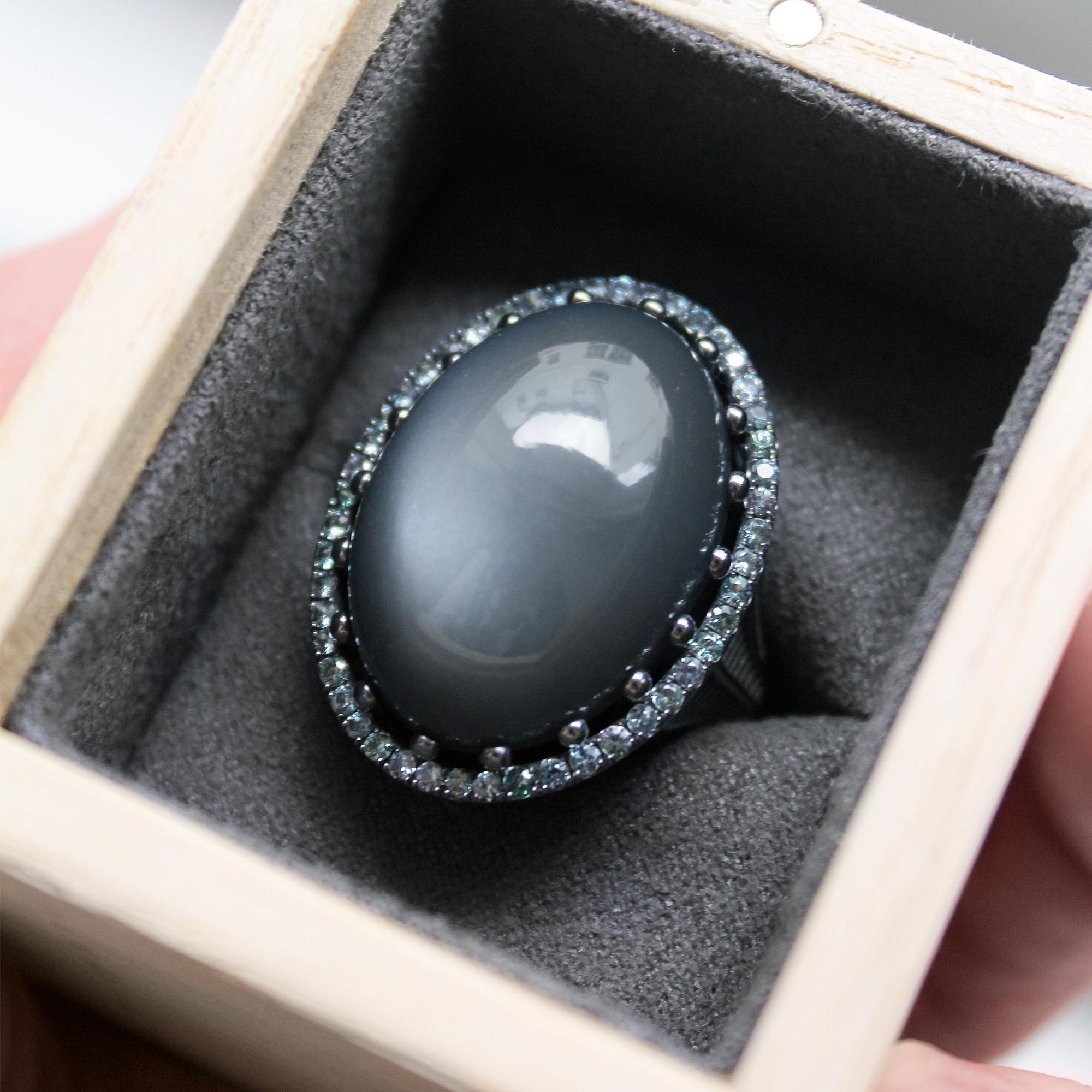 One of a Kind Cabochon Dome Cocktail Ring handmade by jewelry artist Roule and Co in matte-finished 18k black gold featuring a 35.92 carat glowing gray moonstone set in polished black gold ball prongs and surrounded by 0.91 total carats of