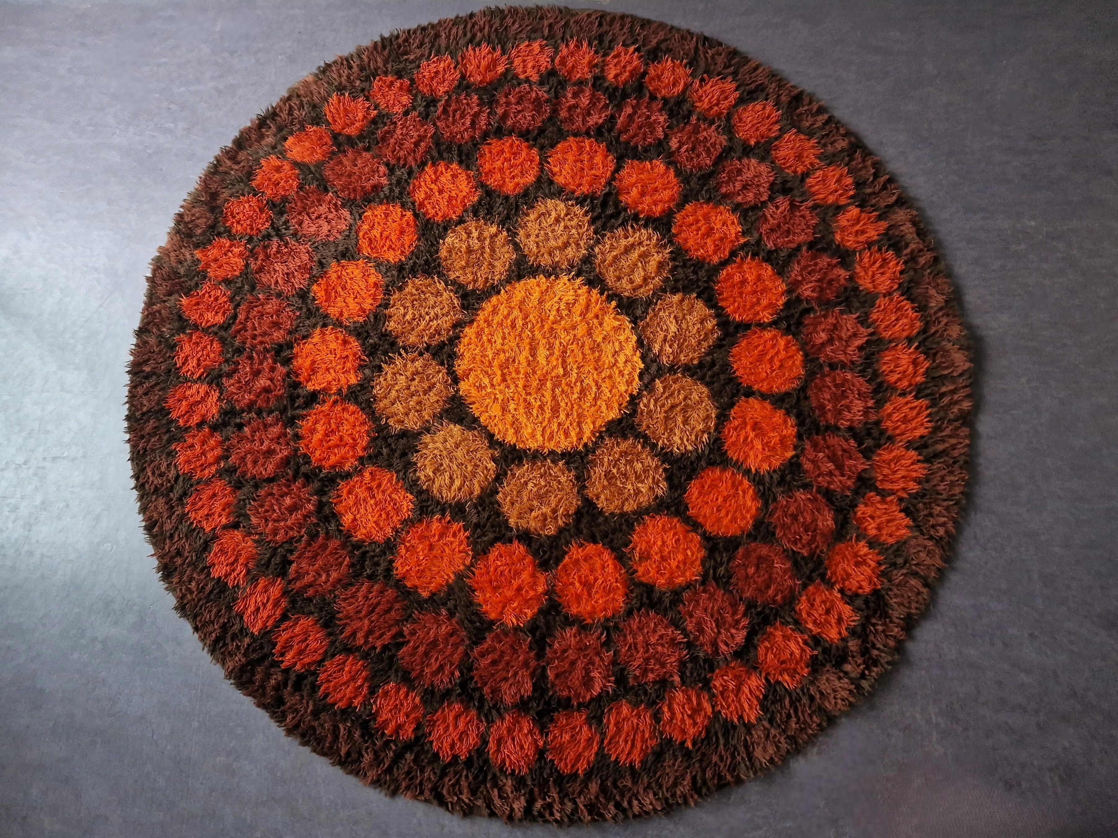Questo tappeto di forma rotonda, modello Roulette, è stato disegnato da Verner Panton per Unika Vaev in Danimarca nel 1965. È realizzato al 100% in lana Rya e presenta un bellissimo motivo giocoso con un cerchio al centro da cui si irradiano cerchi