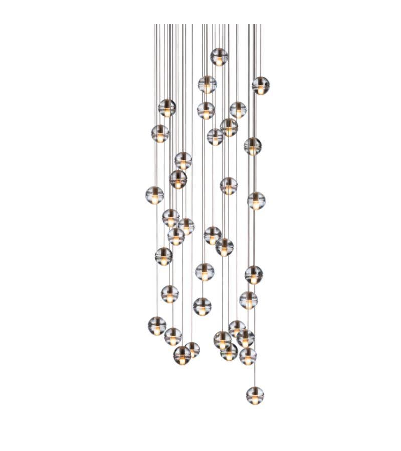 Round 14.36 chandelier lamp by Bocci
Dimensions: Diameter 75.5 x H 300 cm
Materials: Brushed Nickel, Cast glass, blown borosilicate glass, braided metal coaxial cable, electrical components, and white powder-coated canopy.
Available in Square, or