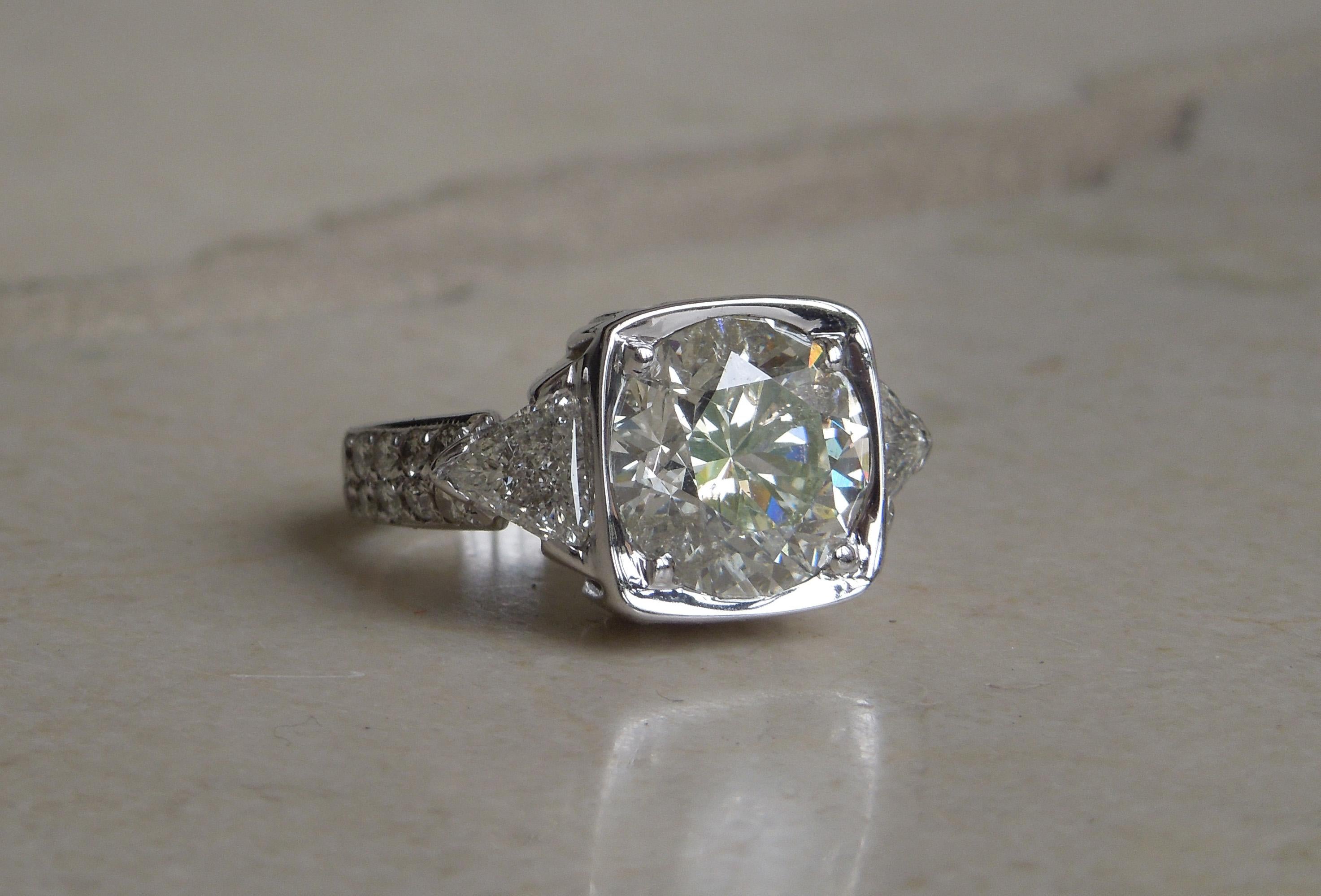 Featuring a central 5.10 carat Round Brilliant cut at 10.8mm in diameter ranking a J Color & I1 Clarity. Facing up extremely white for a J Color, as well as encased in a rounded square encasing creating the optical illusion of a 7 carat Solitaire.
