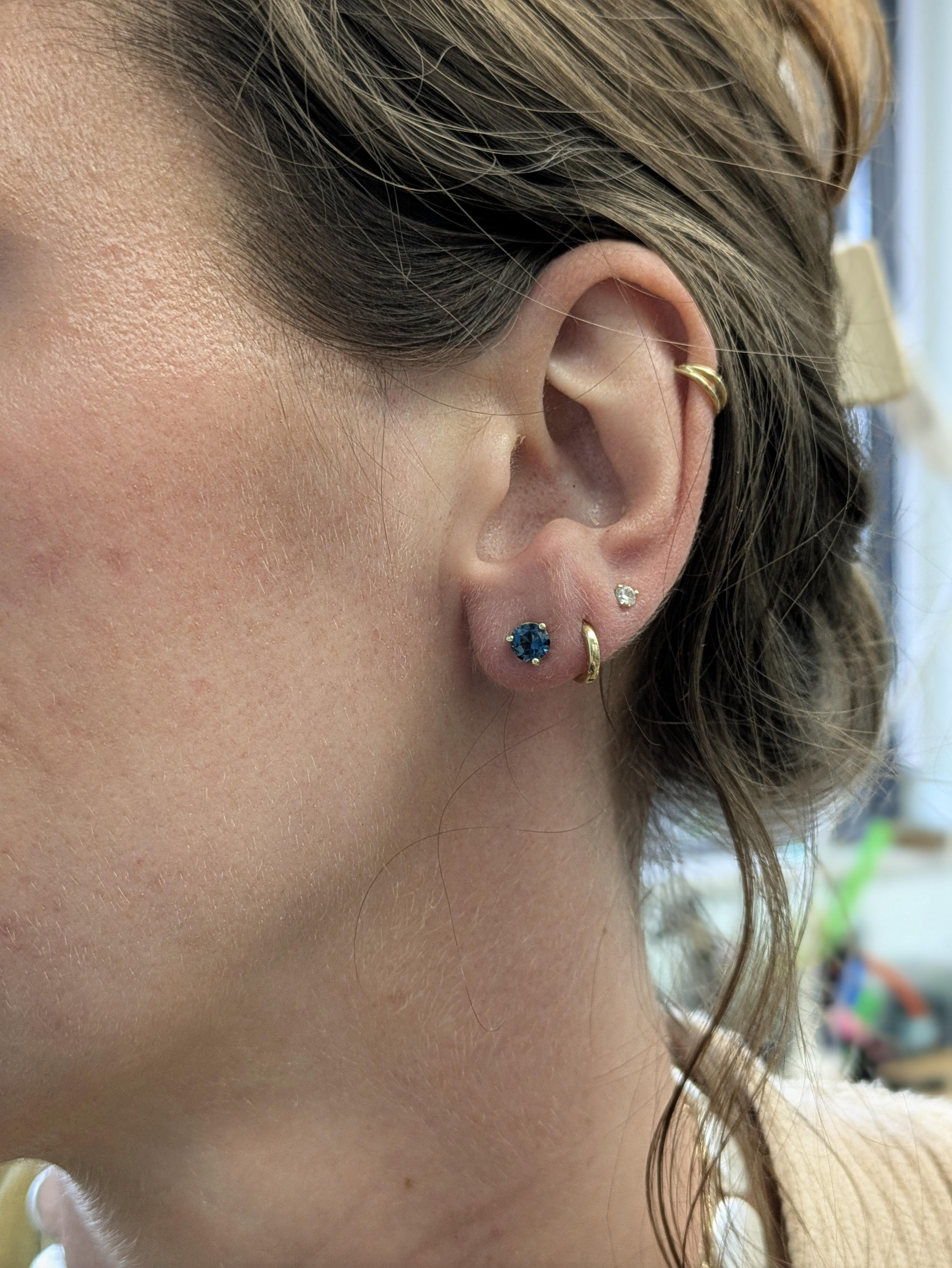 Eleganza profonda per tutti i giorni: queste borchie in oro giallo 14 carati con incastonatura a martini e Topazio Blu di Londra conferiscono al tuo look sfumature oceaniche e ricche. Le gemme rotonde da 5 mm brillano di un lusso sobrio, perfetto