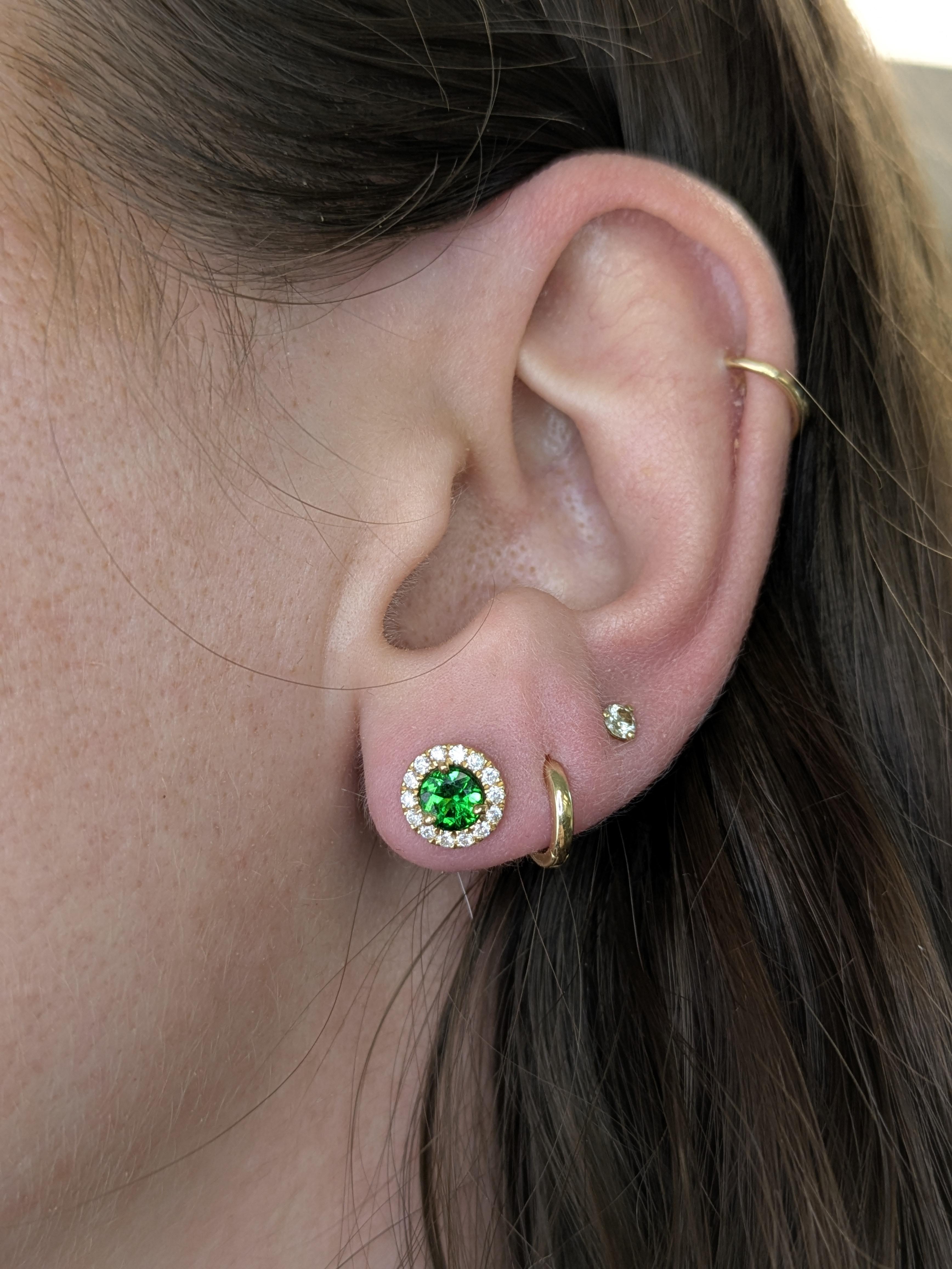 This pair of 5mm round Tsavorite earrings showcases vibrant green gemstones framed by a halo of earth-mined diamonds. Set in solid 14k yellow gold with butterfly backings, they embody timeless fine jewelry elegance.


