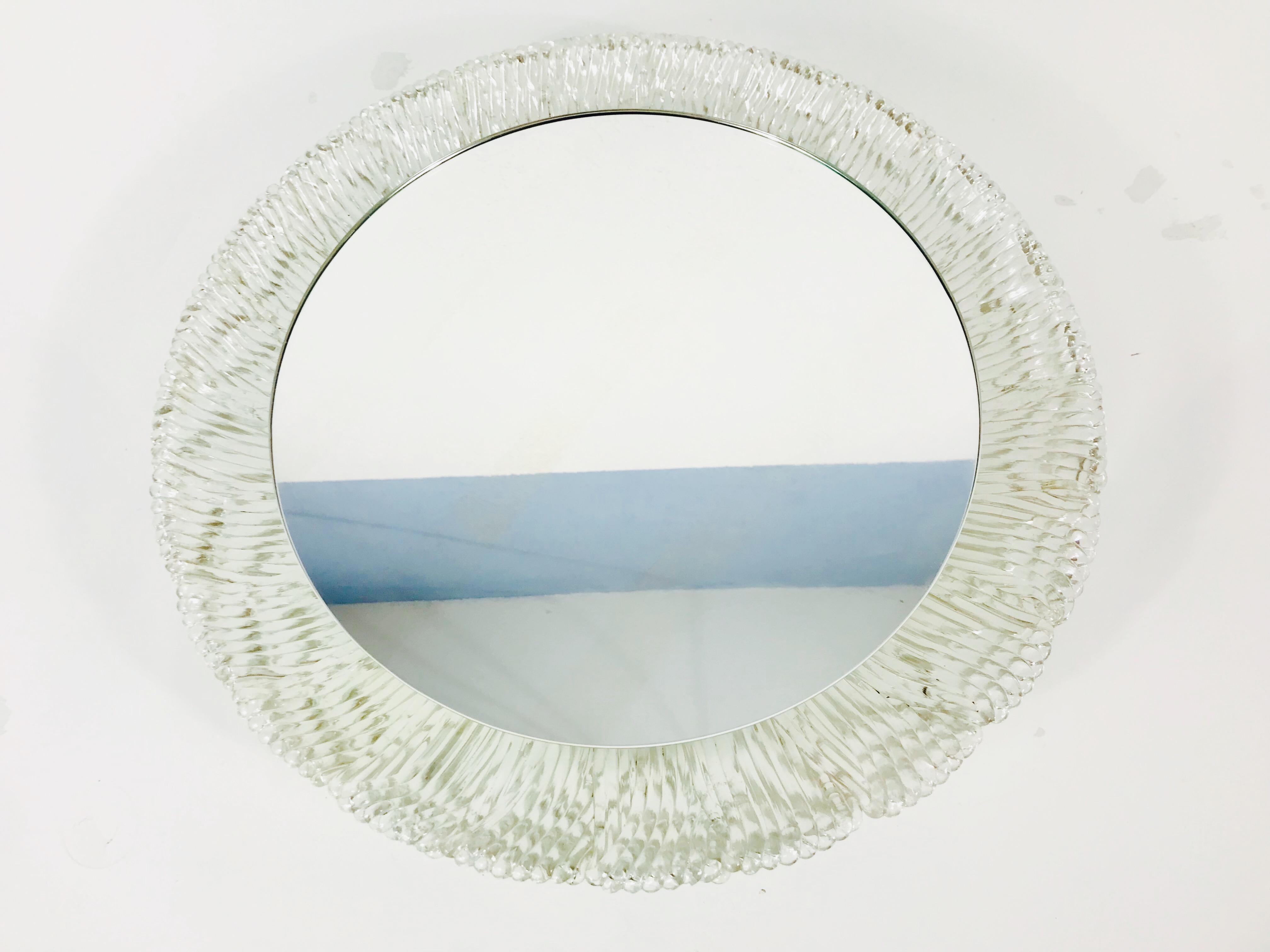An illuminated wall mirror from the German manufacturer Hillebrand Lighting. It was made in the 1970s. The mirror has an oval acrylic design. There are E14 light bulbs inside the frame. The mirror is in a good vintage condition.