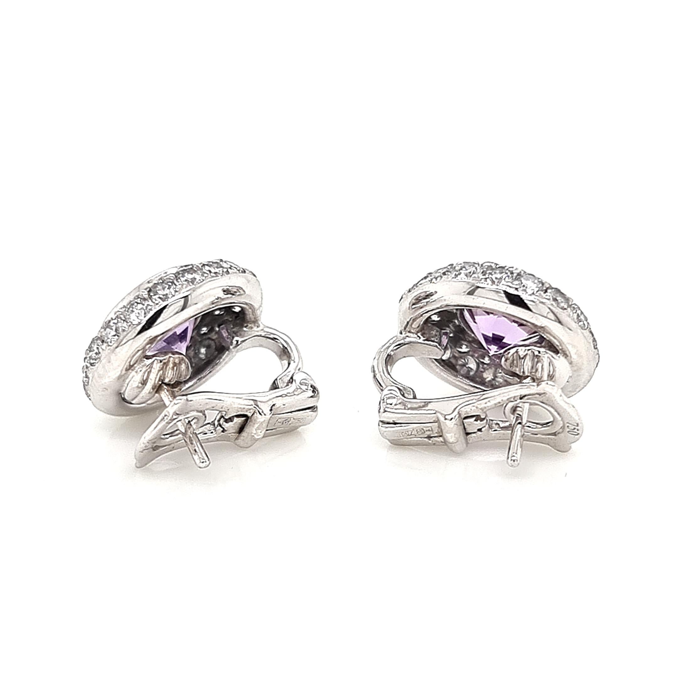 Indulge in the allure of these elegant earrings, meticulously crafted from opulent 18K white gold. At their center lies a resplendent round amethyst, exuding a regal purple hue that captivates the beholder. The amethysts are embraced by a halo of