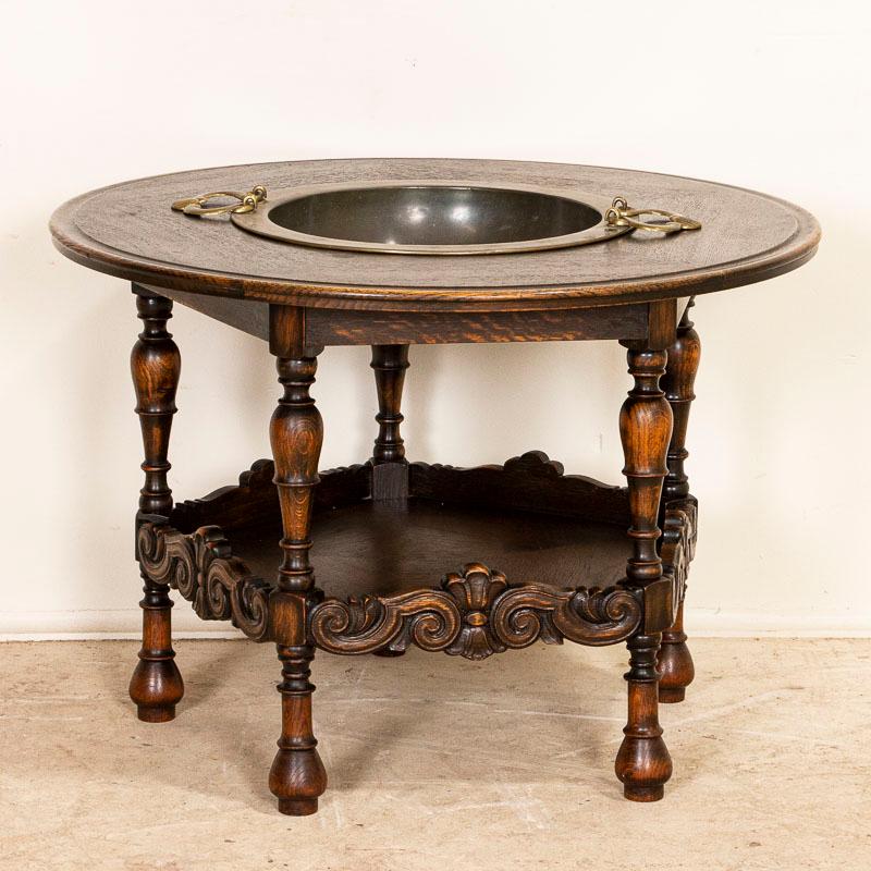 This antique oak coffee table from Denmark with a removeable brass tray insert originally served as a type of large ash tray. With 5 turned legs and ornately carved aprons, this unique piece may be creatively used for a variety of hosting in today's