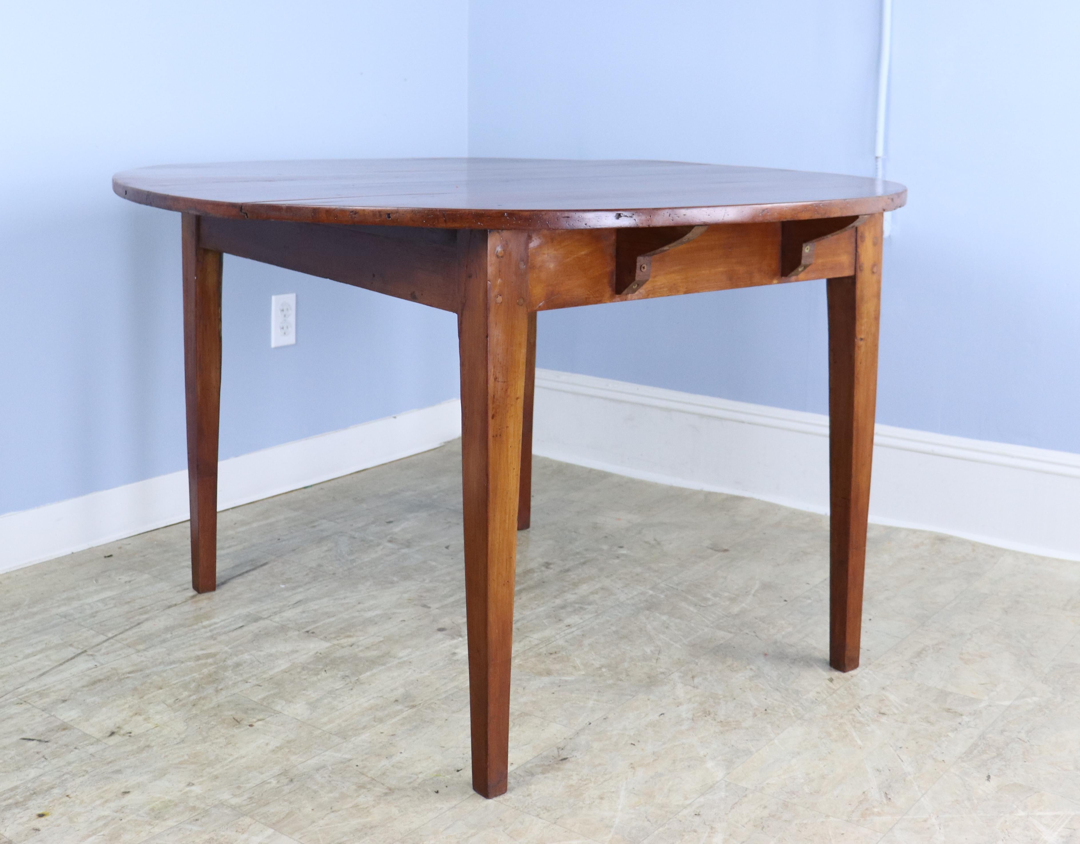 An antique thick topped dining farm table from France. Made of fruitwood with a rich color and patina, with areas of moderate distress. A good-sized breakfast table. Lovely farm table tapered legs. Note that the top is not a perfect circle (though