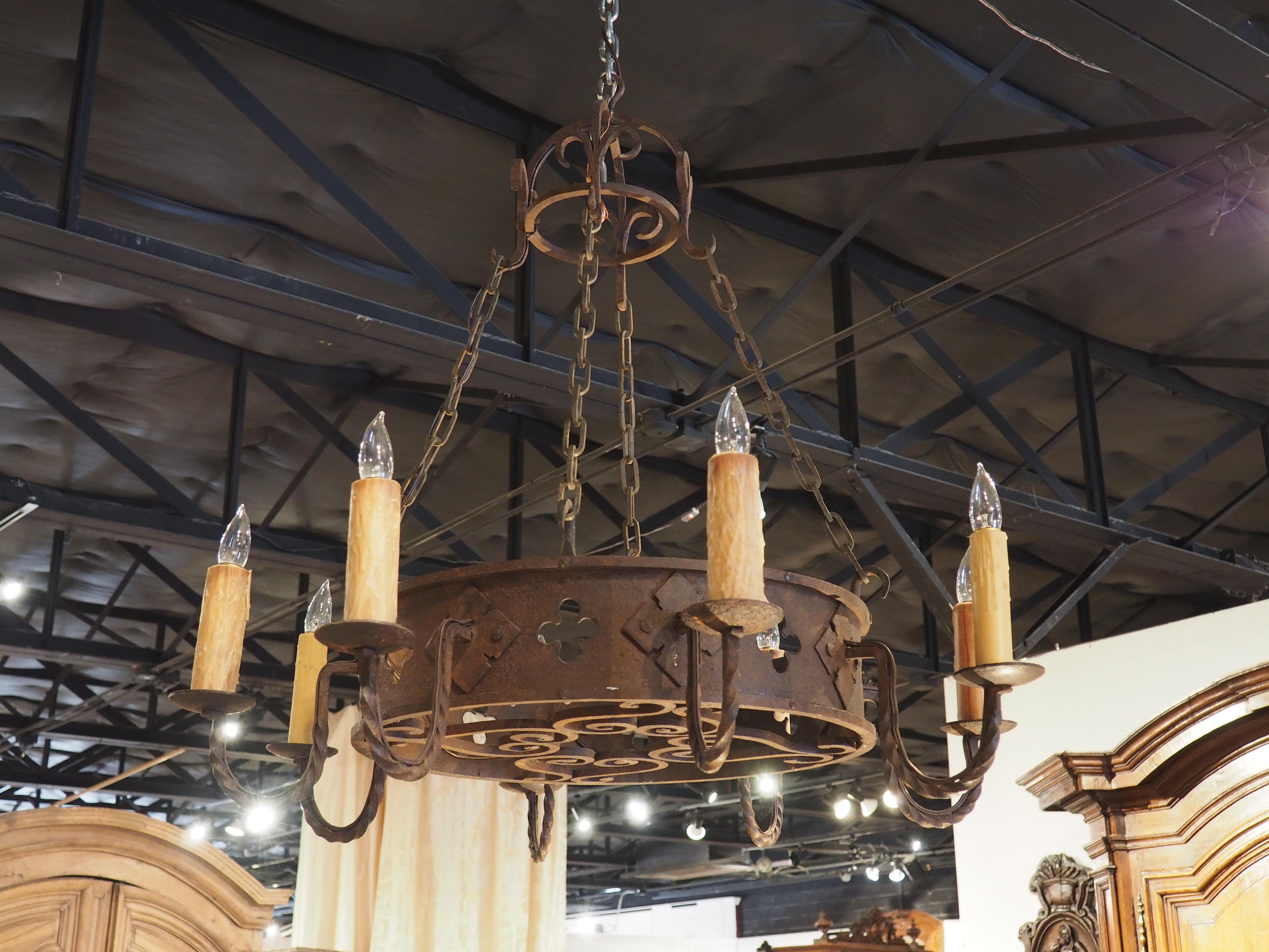 This antique French round iron chandelier has a tall metal band of rusted iron with eight candlelight arms around the outside. The arms are scooped with a twisted motif and have a back plate of a four sided floret. In between the arms on the band