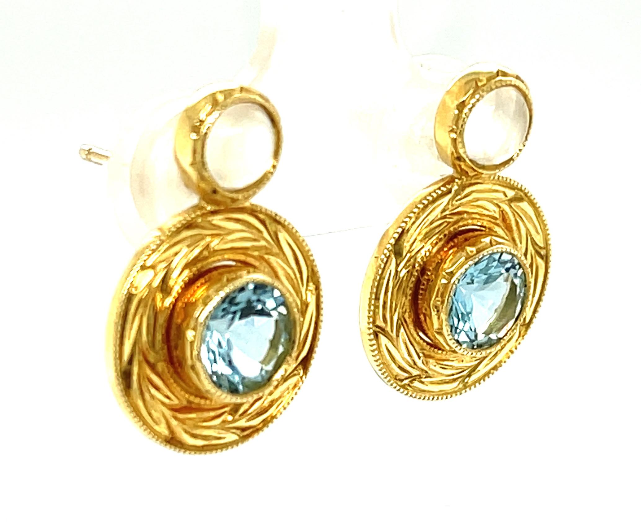 These beautiful earrings feature sparkling blue aquamarine gemstones and luminous moonstone cabochons set in 18k yellow gold bezels. The aquamarine settings have hand-engraved yellow gold frames that add sophisticated style and a luxurious touch to