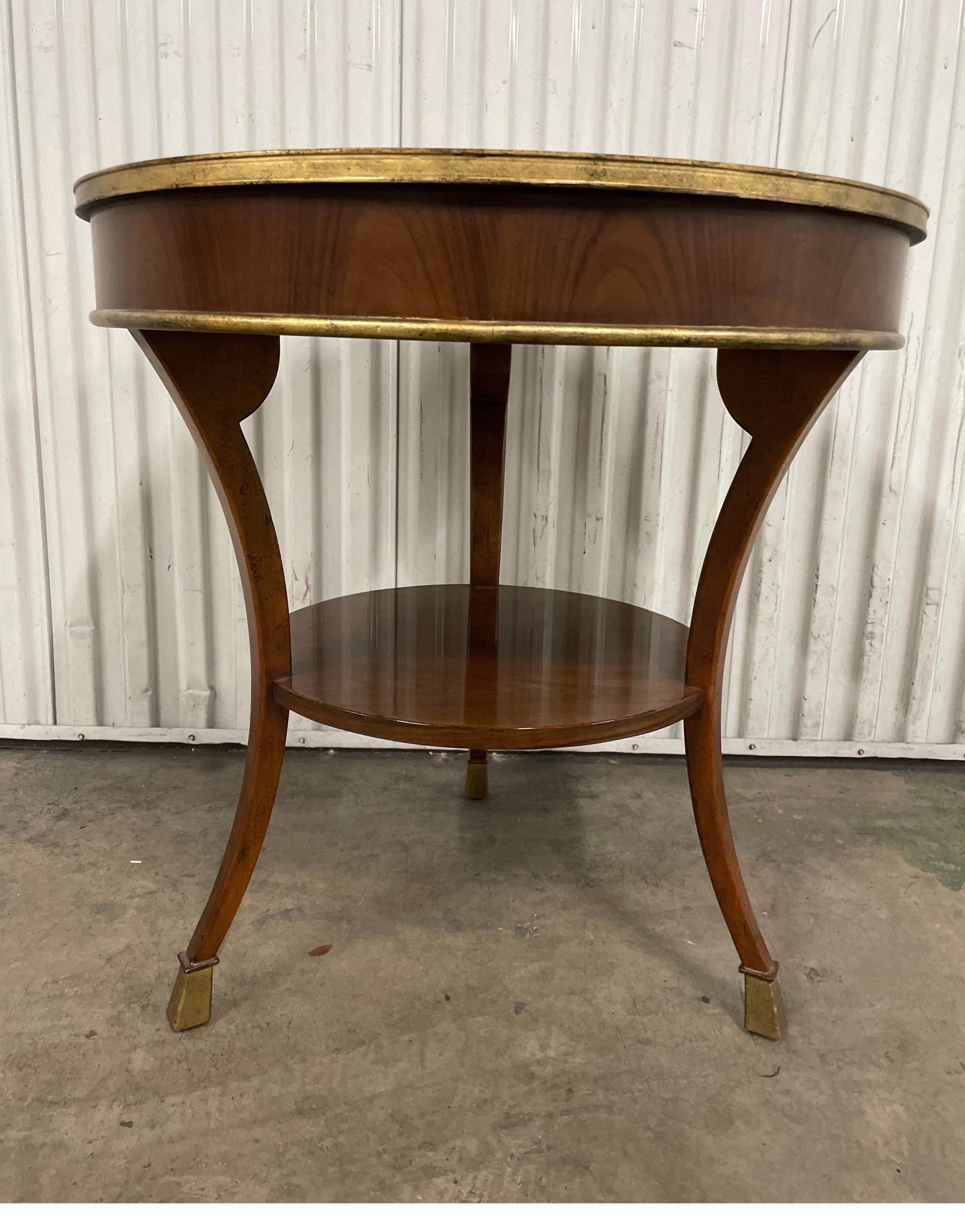 Round two-tiered Art Deco style side table by Baker Furniture Company. Gilded rims & feet.